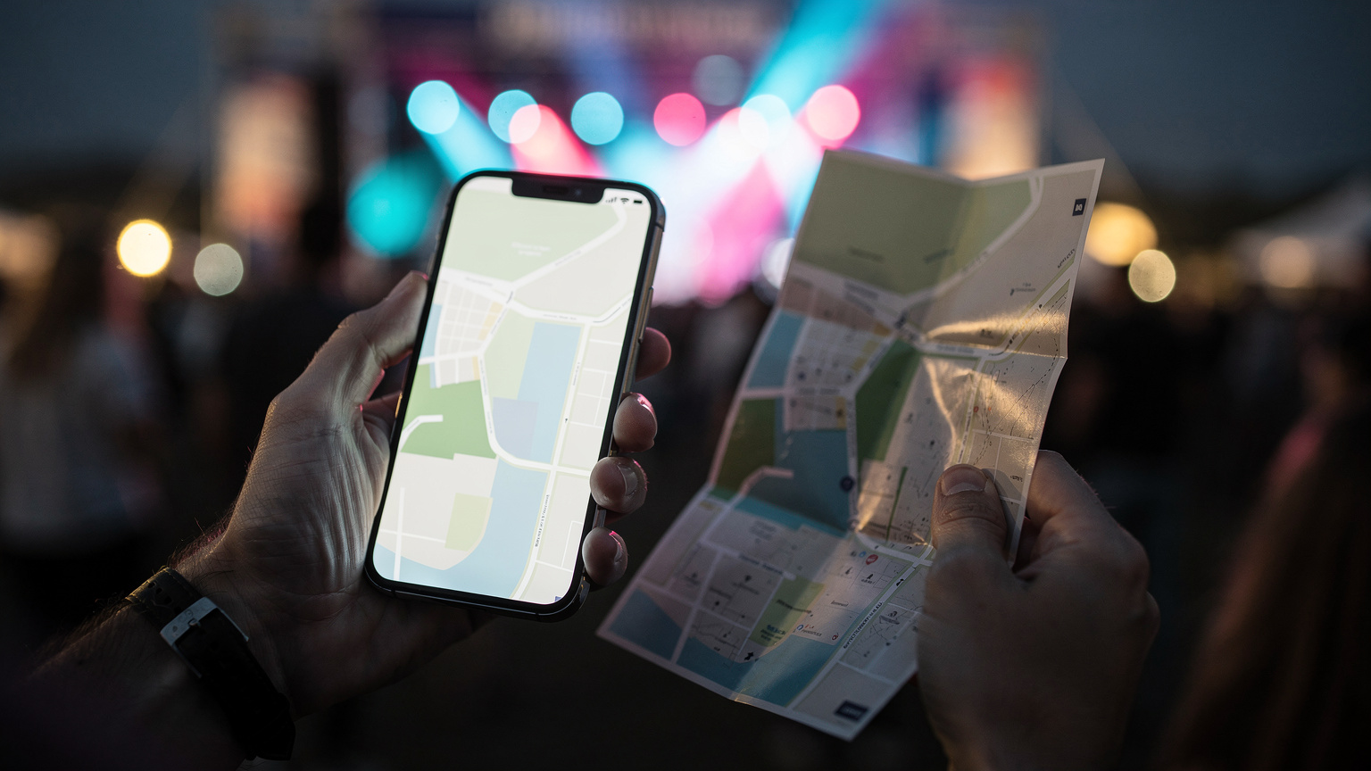 Κοντινό πλάνο σε χέρια που κρατούν ένα smartphone και ένα χάρτη φεστιβάλ, με το φόντο να δείχνει θολά φώτα από τη σκηνή.