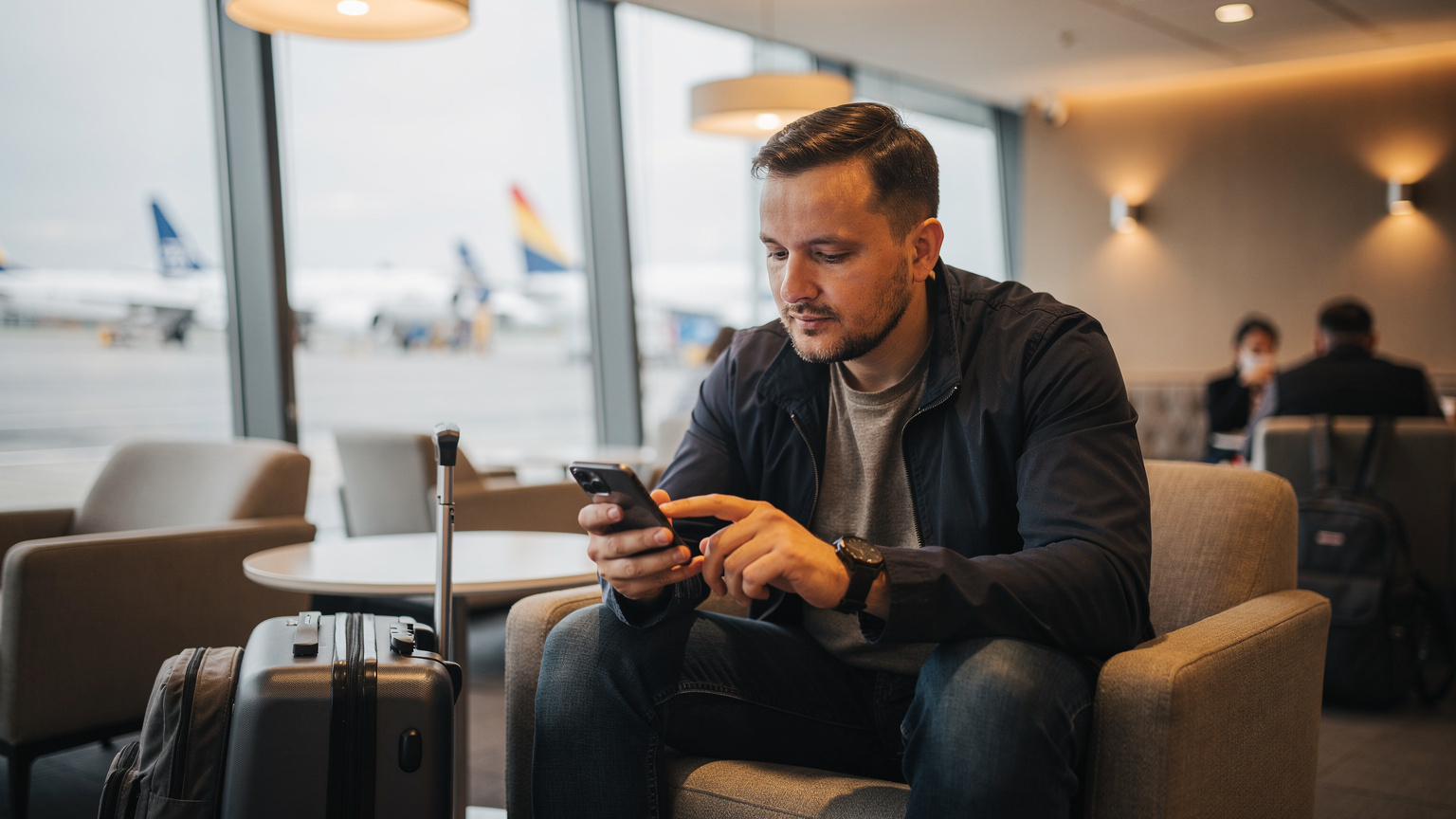 Український мандрівник налаштовує eSIM на своєму смартфоні, сидячи у затишному лаунжі аеропорту Шопена у Варшаві, готуючись до відльоту.