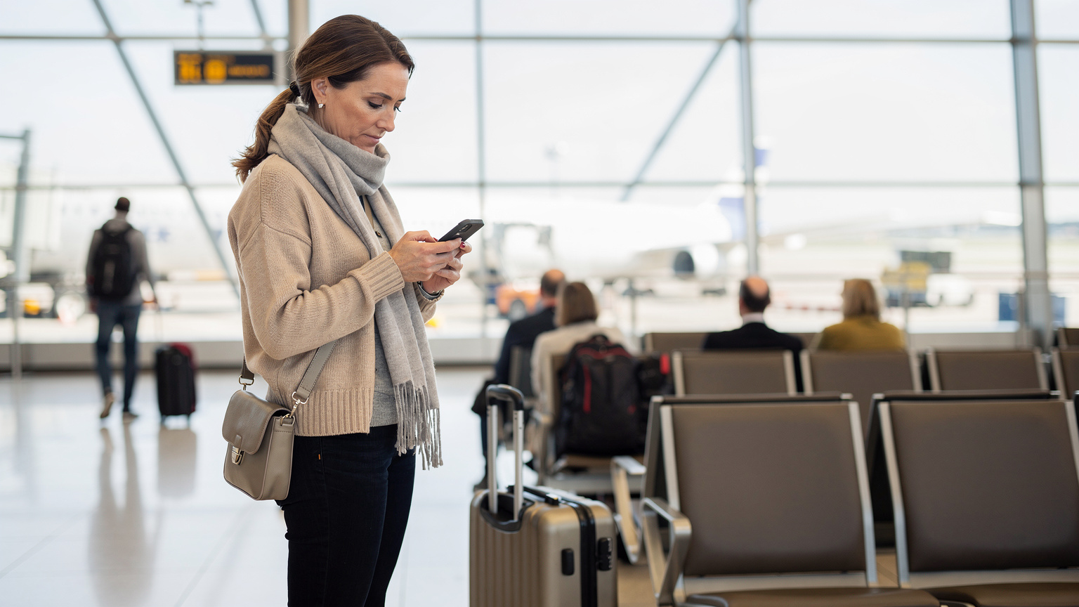 En travel reisende sjekker kartet på telefonen sin, mens bagasjen ligger klar ved siden av. Hun planlegger den neste etappen av reisen, kanskje med et blikk på en regional eSIM.