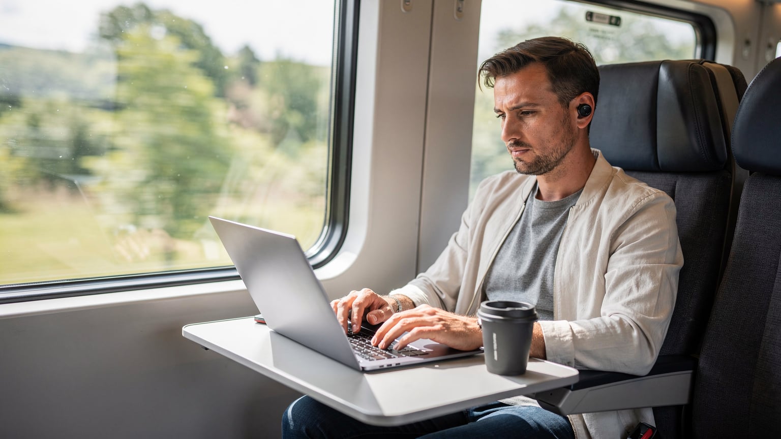 A traveler uses their laptop with an active eSIM connection, enjoying seamless internet access while riding on a high-speed train, watching the countryside blur past the window.