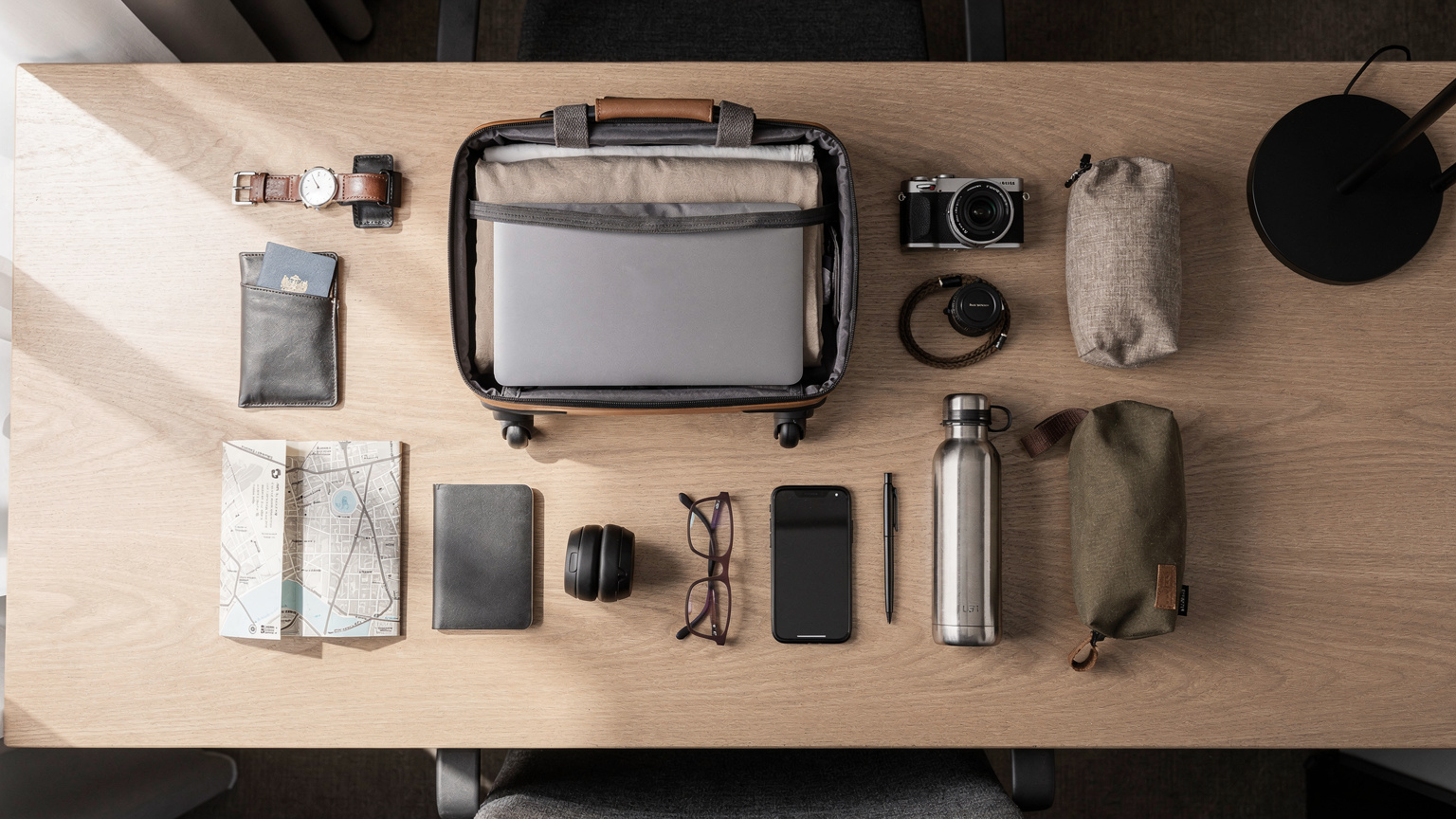 An overhead flat-lay of a minimalist travel setup: a smartphone, passport, noise-canceling headphones, and a small, neatly folded city map on a hotel desk, emphasizing preparation.