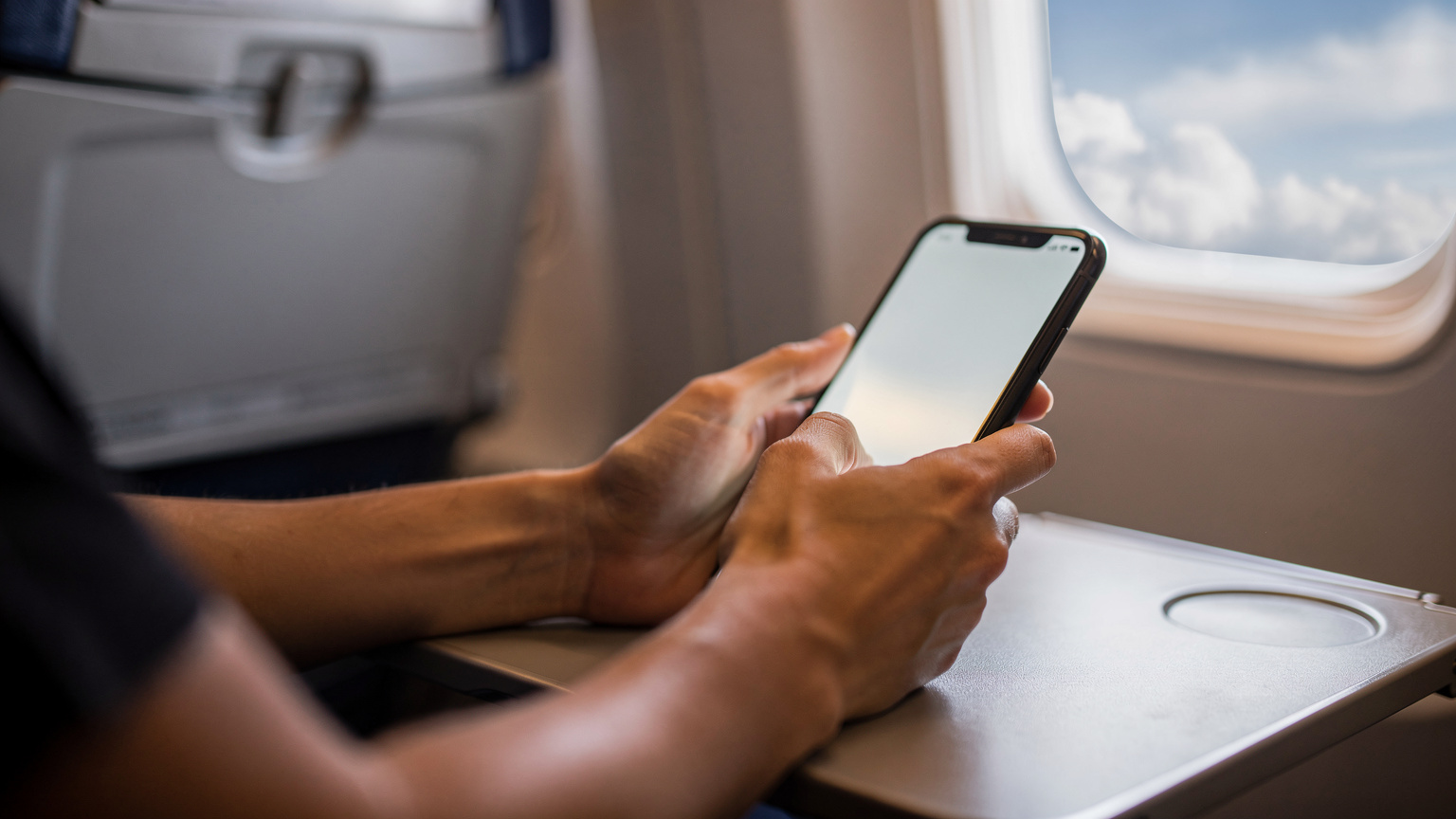 Zblízka pohled na ruce cestovatele, který na svém smartphonu porovnává eSIM datové balíčky pro Kapverdy, s rozmazaným pozadím palubní desky letadla.