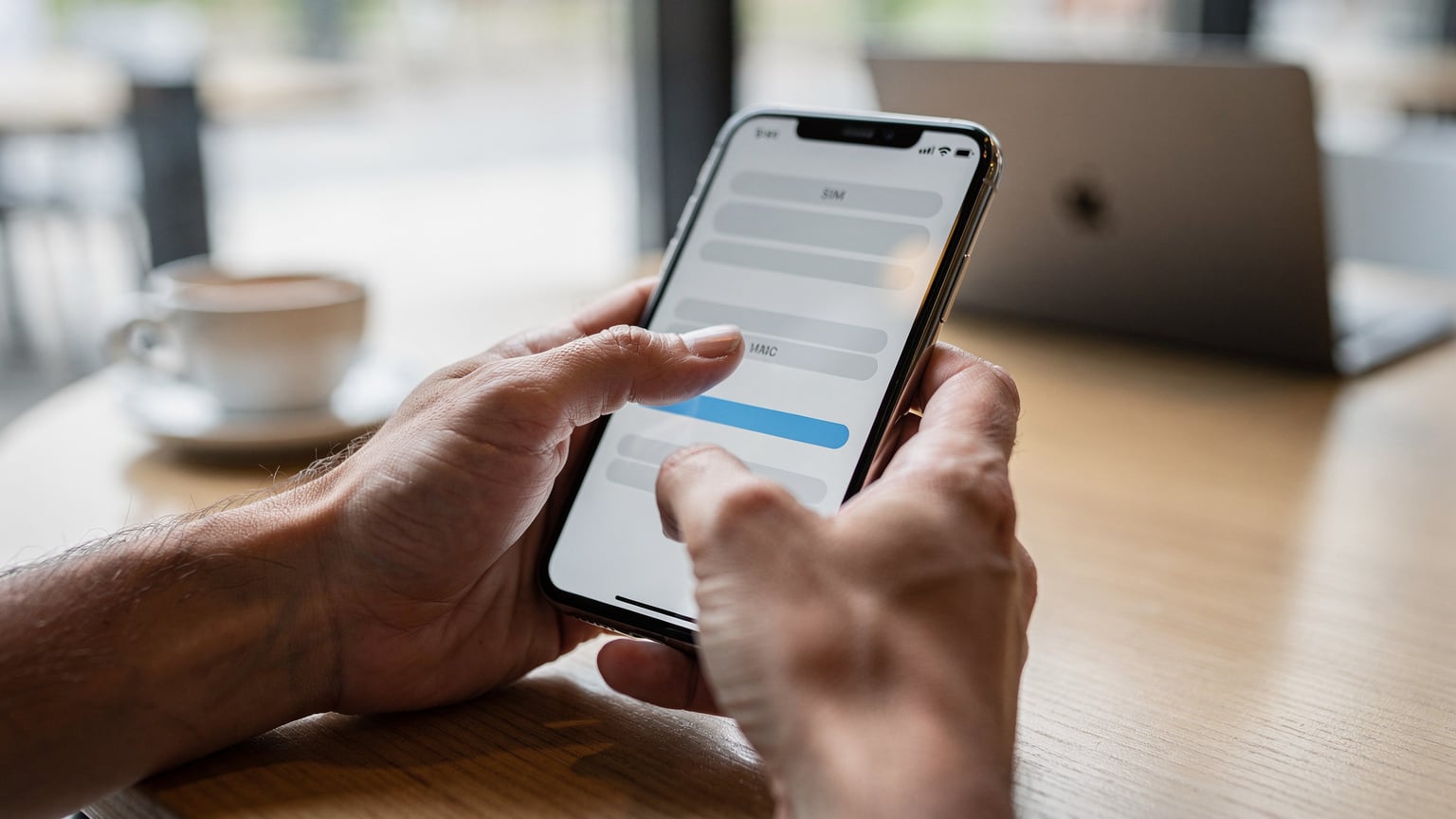Primer plano de manos adultas configurando una eSIM en un iPhone, con la pantalla mostrando el proceso de instalación de un perfil, en un entorno luminoso de cafetería.