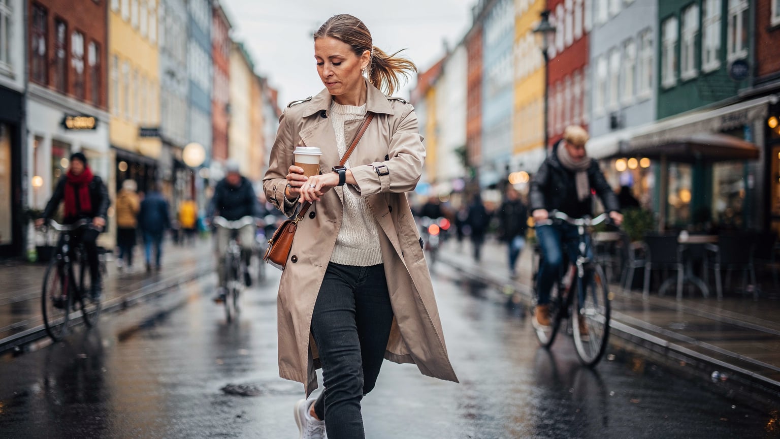 En kvinde navigerer travle gader i København, tjekker sit Apple Watch for notifikationer, mens hun holder en kaffekop.
