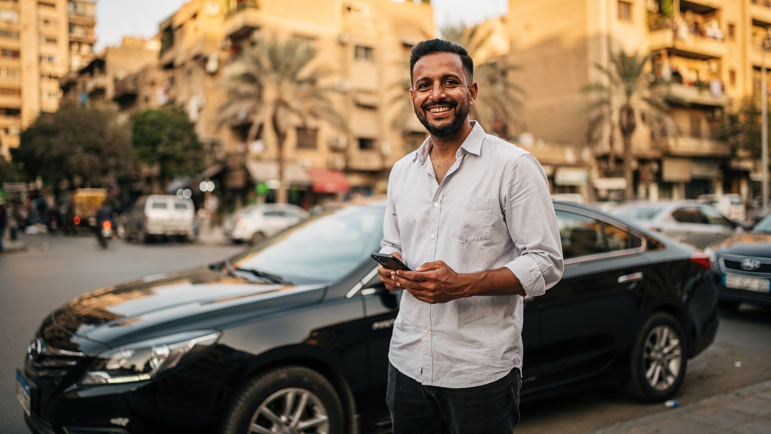 Un homme souriant, un téléphone à la main, devant un taxi Careem ou Uber au Caire, illustrant la facilité de navigation et de transport grâce à une eSIM.