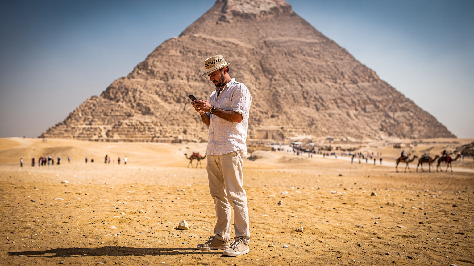 Un homme consulte son téléphone devant les pyramides de Gizeh, cherchant la meilleure offre eSIM pour son voyage en Égypte.