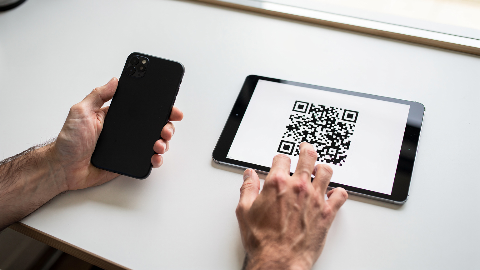 Nahaufnahme von Händen, die ein Smartphone über ein Tablet halten, um einen QR-Code zu scannen, der zur Installation einer eSIM dient.