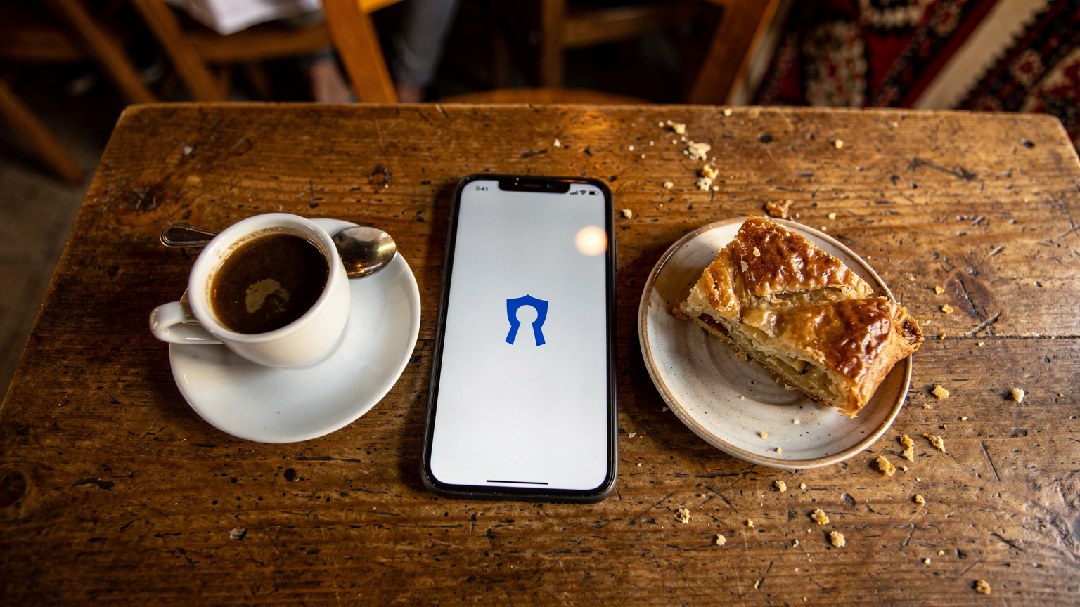 Ein Smartphone mit einer geöffneten VPN-App liegt auf einem Tisch in einem albanischen Café neben einem traditionellen Kaffee und Gebäck.