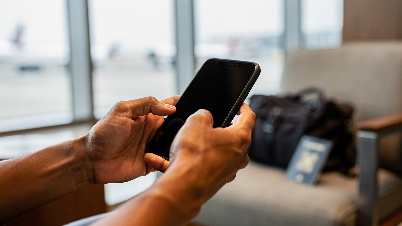 Close-up of a traveler's hands holding a smartphone, with blurred background, showing the gesture of scanning a QR code for eSIM activation, no screen content visible.