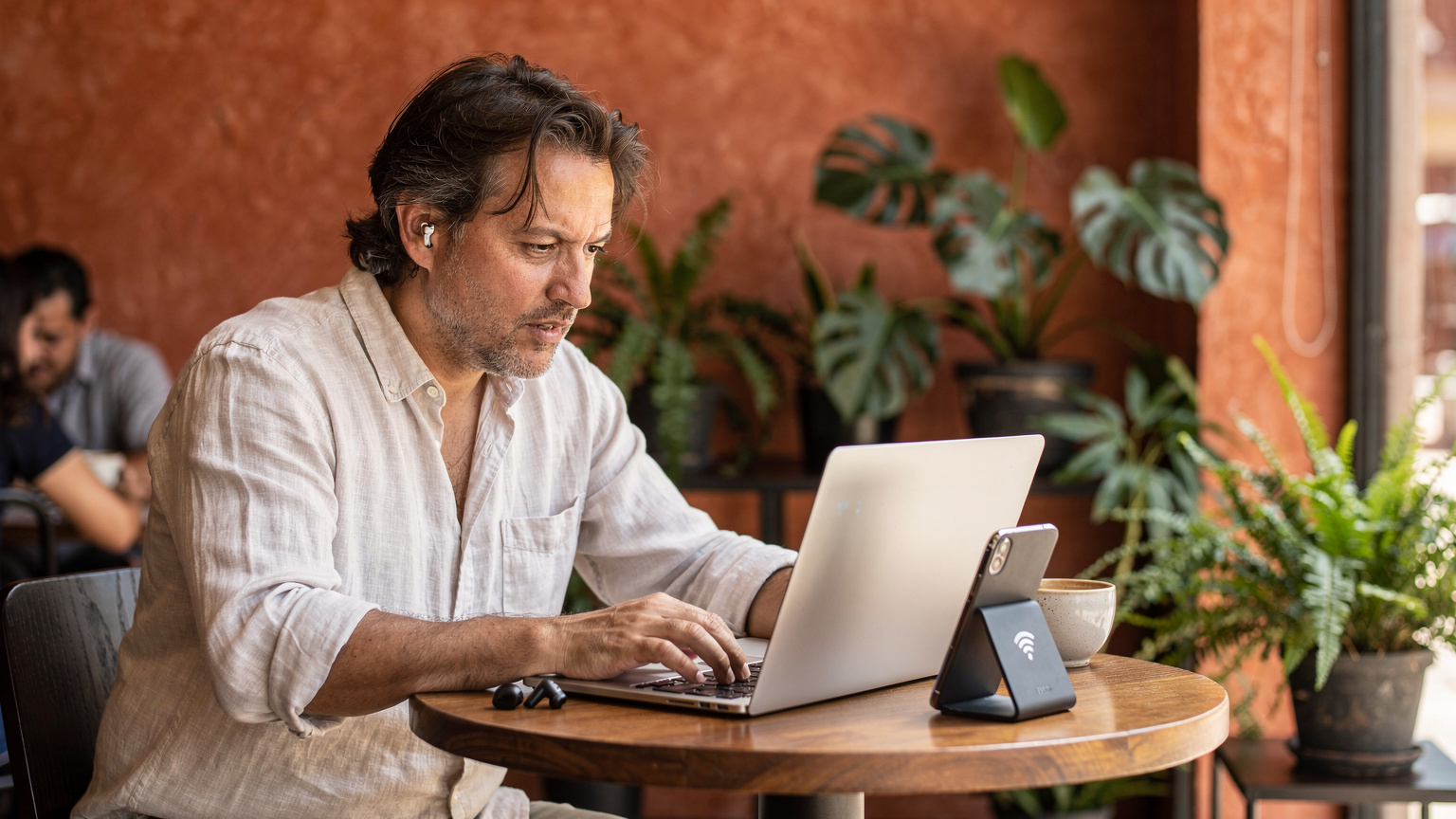 Ein Digitaler Nomade arbeitet in einem belebten Café in Mexiko-Stadt an seinem Laptop, mit einem Smartphone neben ihm für Hotspot-Nutzung.
