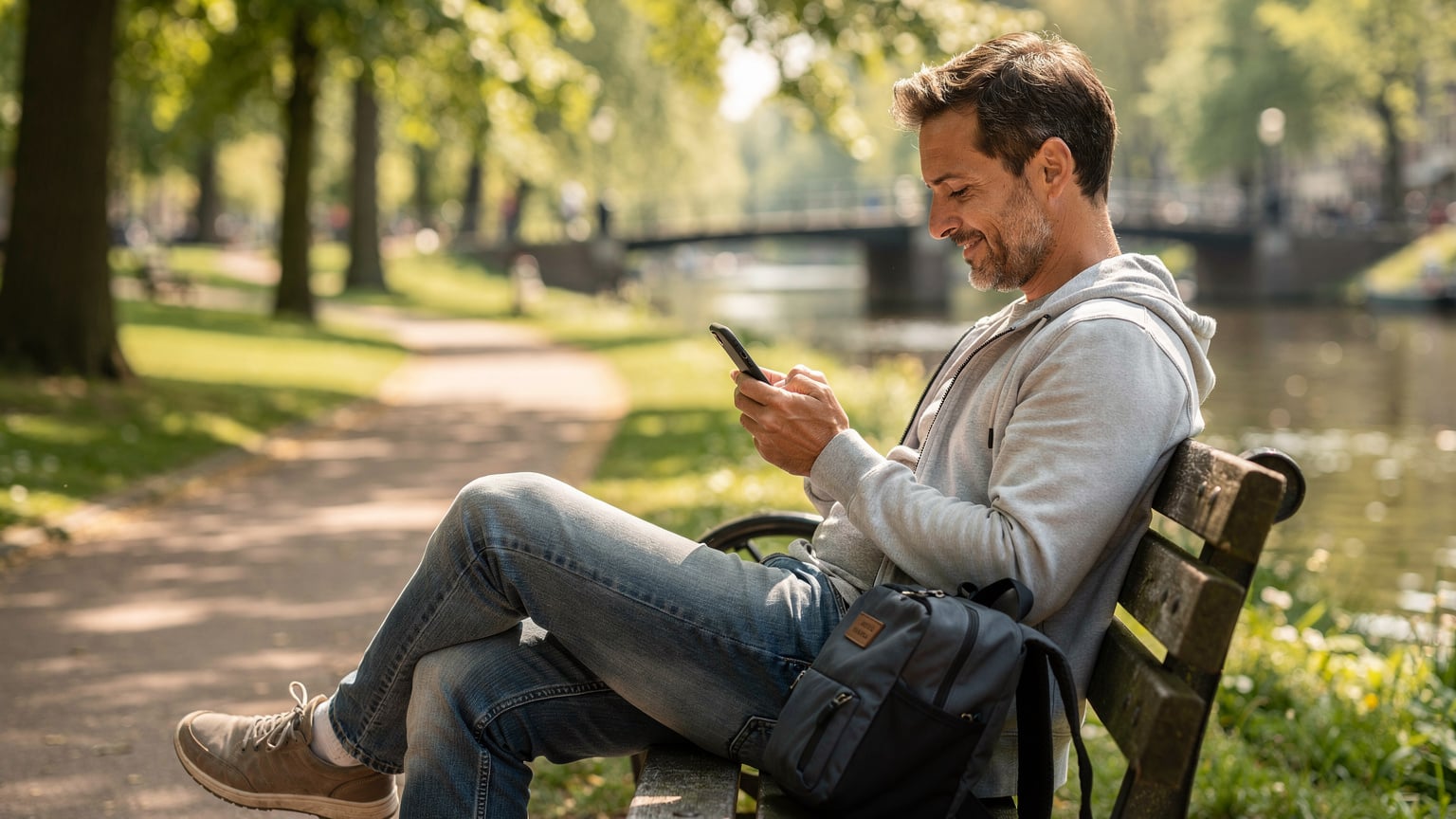 Een reiziger controleert de instellingen van zijn smartphone om het dataverbruik te monitoren, zittend op een bankje in het Vondelpark in Amsterdam.