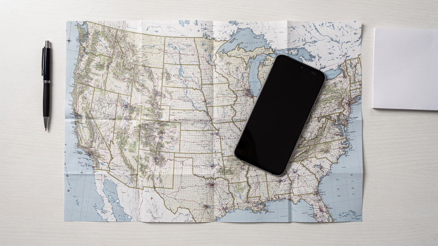 Un téléphone portable posé sur une carte routière détaillée du Canada, avec un passeport, des lunettes de soleil et des écouteurs à côté, symbolisant la préparation minutieuse d'un road trip.