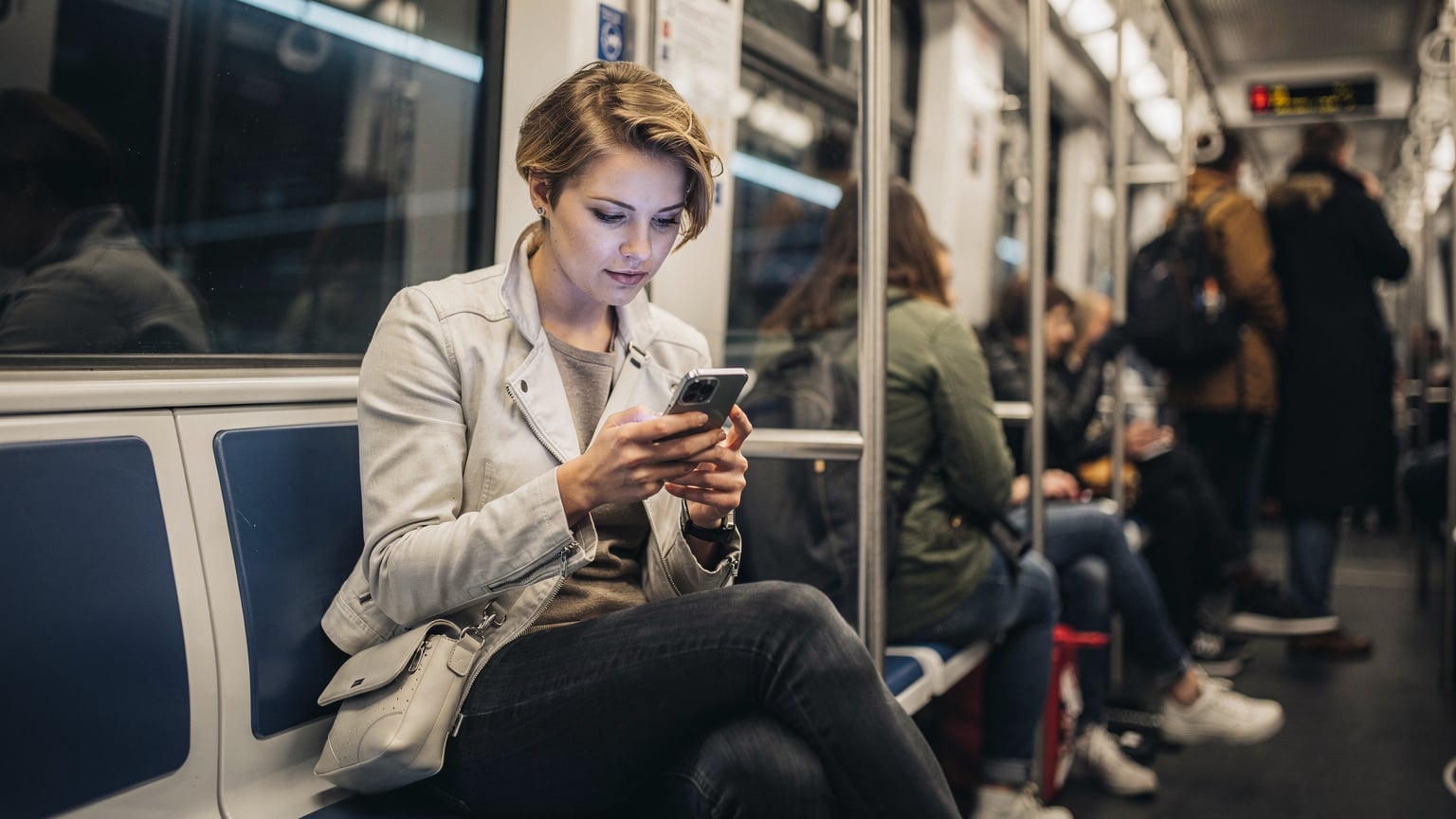 En kvinde sidder på en travl metro i København, med sin telefon i hånden og et koncentreret udtryk, mens hun tjekker forbindelsen på sin enhed.