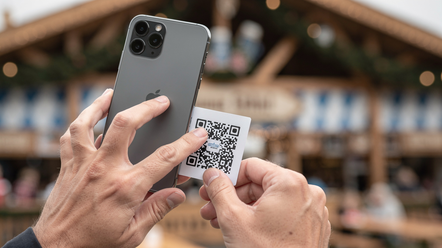 Ein Detailfoto von Händen, die ein Smartphone halten und einen QR-Code scannen, um eine eSIM zu aktivieren, mit unscharfem Oktoberfest-Hintergrund.