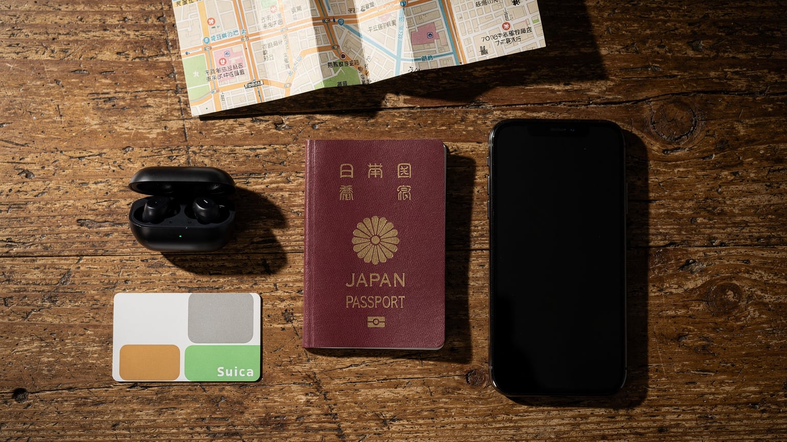 パスポート、スマートフォン、ワイヤレスヘッドホン、現地の交通カードが置かれた旅行者のテーブル。