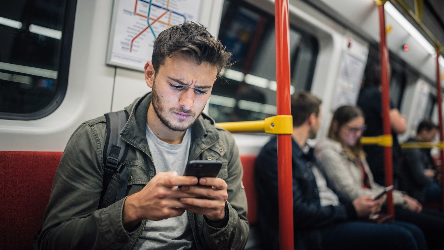 A traveler looks at their phone screen with a slight frown, indicating a potential connectivity issue or data warning, while sitting on a train in the London Underground.
