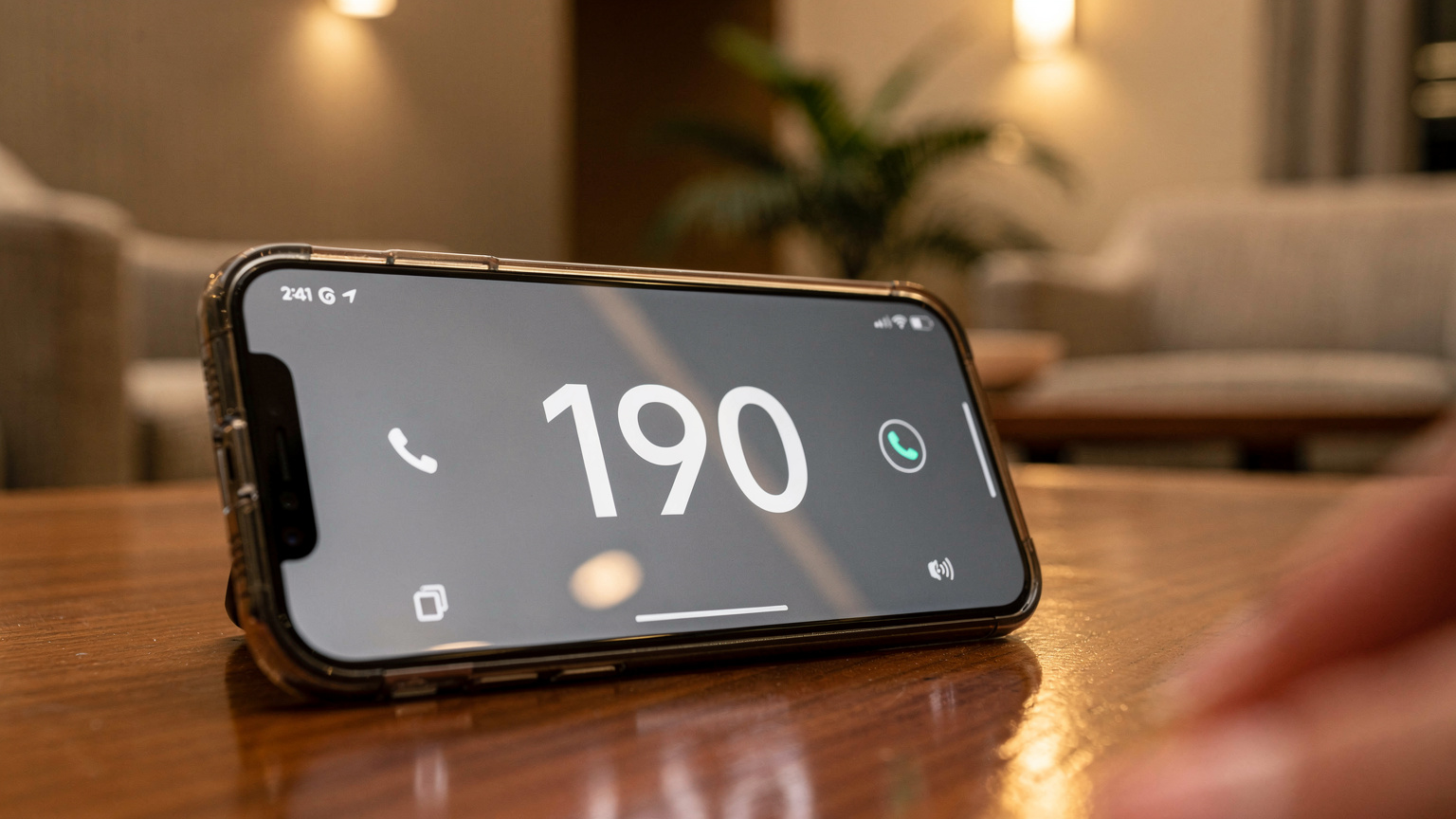 Gros plan sur un smartphone affichant l'écran d'appel avec le numéro 190 (police brésilienne) composé, posé sur une table basse dans le hall d'un hôtel brésilien. L'ambiance est sérieuse et pressante.