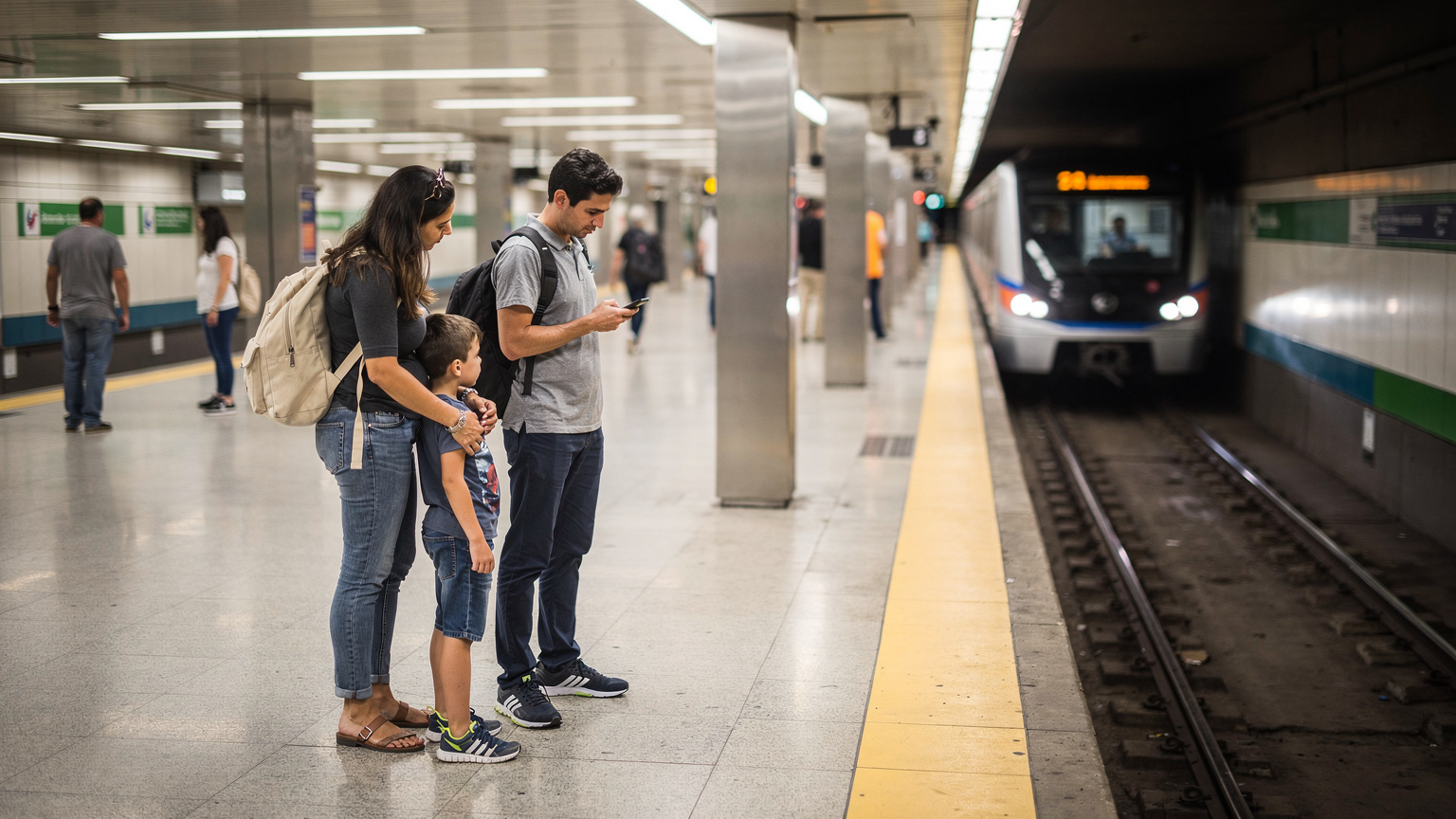 Une famille (deux parents, deux enfants) attend sur un quai de métro moderne à São Paulo. Le train est visible en arrière-plan, et l'ambiance est propre et ordonnée. Un parent tient la main d'un enfant pendant que l'autre consulte son téléphone.