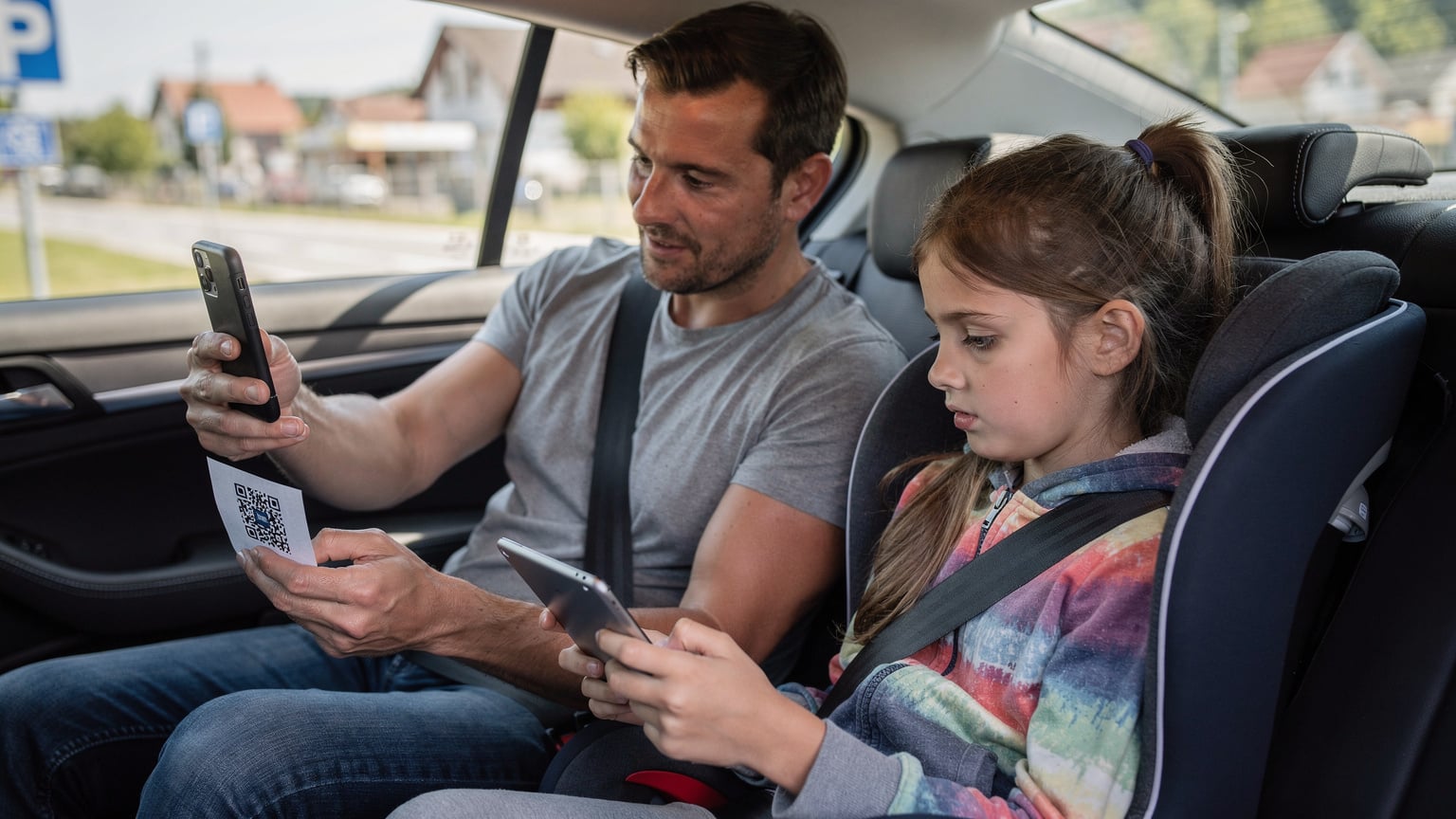 Een vader zit op de achterbank van een auto, scant een QR-code op zijn smartphone om een eSIM te installeren, terwijl zijn 8-jarige dochter naast hem geconcentreerd naar een tablet kijkt.
