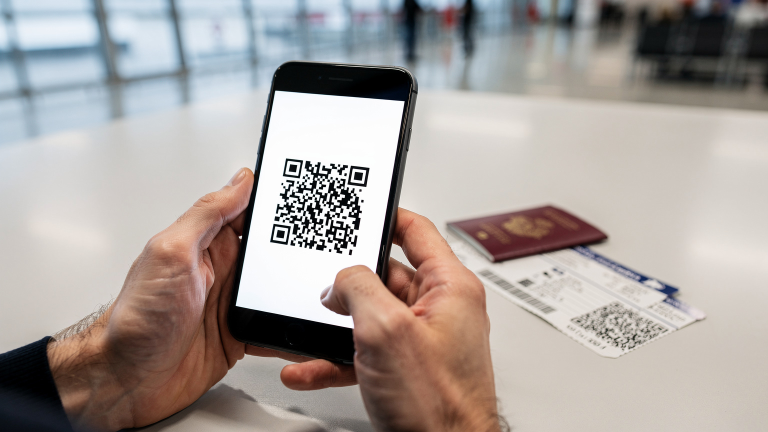 Gros plan sur des mains tenant un smartphone affichant un QR code d'eSIM, avec un passeport ouvert et des billets d'avion en arrière-plan flou, symbolisant une activation rapide avant le départ.