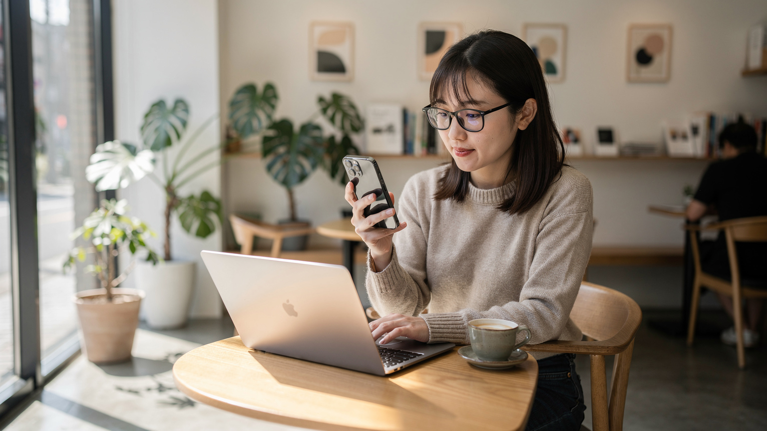 カフェでノートPCとスマートフォンを使いながら、eSIMプランを比較検討する旅行者の様子。