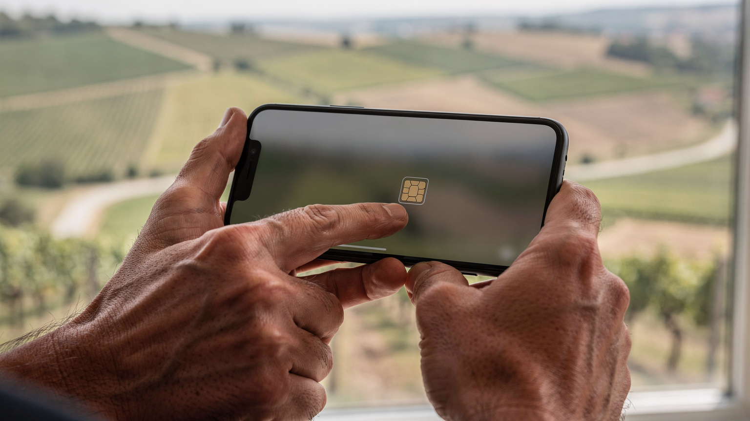 Detailní záběr rukou cestovatele, který drží smartphone a gestem prstu aktivuje eSIM, zatímco v rozostřeném pozadí je vidět mapa jižní Moravy.