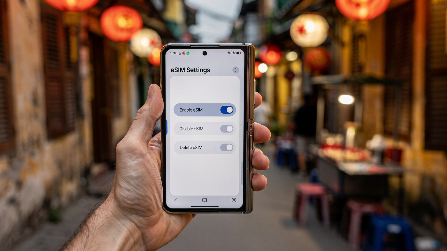Một bàn tay đang cầm điện thoại Samsung Galaxy Z Fold 7 mở ra, hiển thị màn hình cài đặt eSIM với các tùy chọn bật/tắt và xóa eSIM, với cảnh một ngõ nhỏ ở phố cổ Hà Nội có đèn lồng và gánh hàng rong mờ ở hậu cảnh.