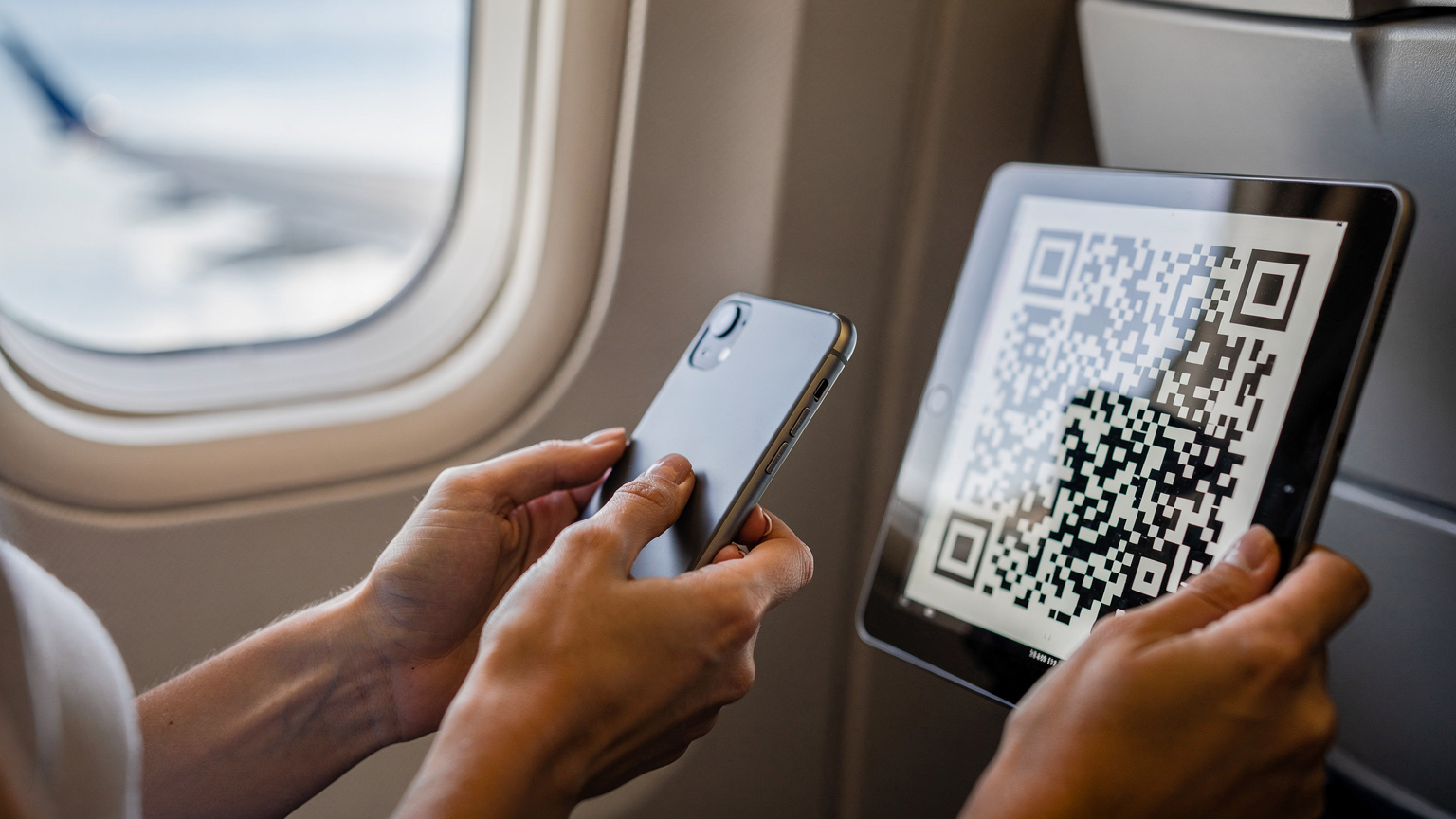 Bir annenin elinde akıllı telefon, Cellesim uygulamasından QR kodu tarayarak uçağın penceresinden görünen kanat manzarası eşliğinde çocuğunun tabletine eSIM kuruyor.