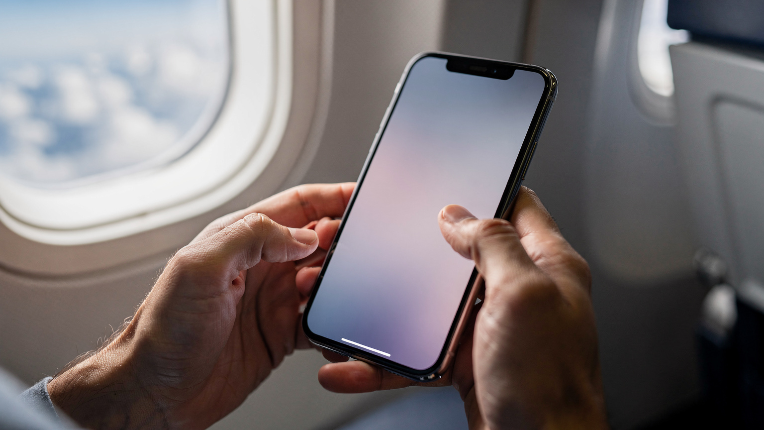 A close-up of human hands activating an eSIM on a smartphone, with a blurred background of a plane window and clouds, suggesting immediate connectivity upon landing.