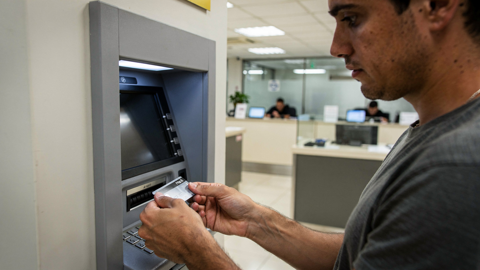 Ein Reisender zeigt seine Kreditkarte an einem ATM in Brasilien, während er vorsichtig die Umgebung beobachtet, um potenzielle Betrüger zu erkennen.
