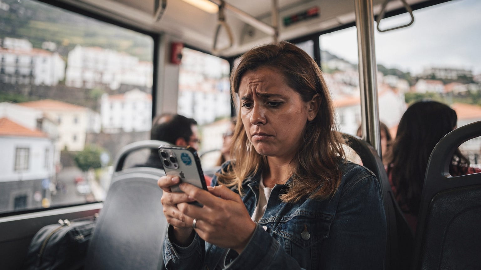 Uma mulher com expressão frustrada, a segurar o seu telefone num teleférico ou transporte público em Funchal, Madeira, com o ecrã a mostrar má receção de rede.