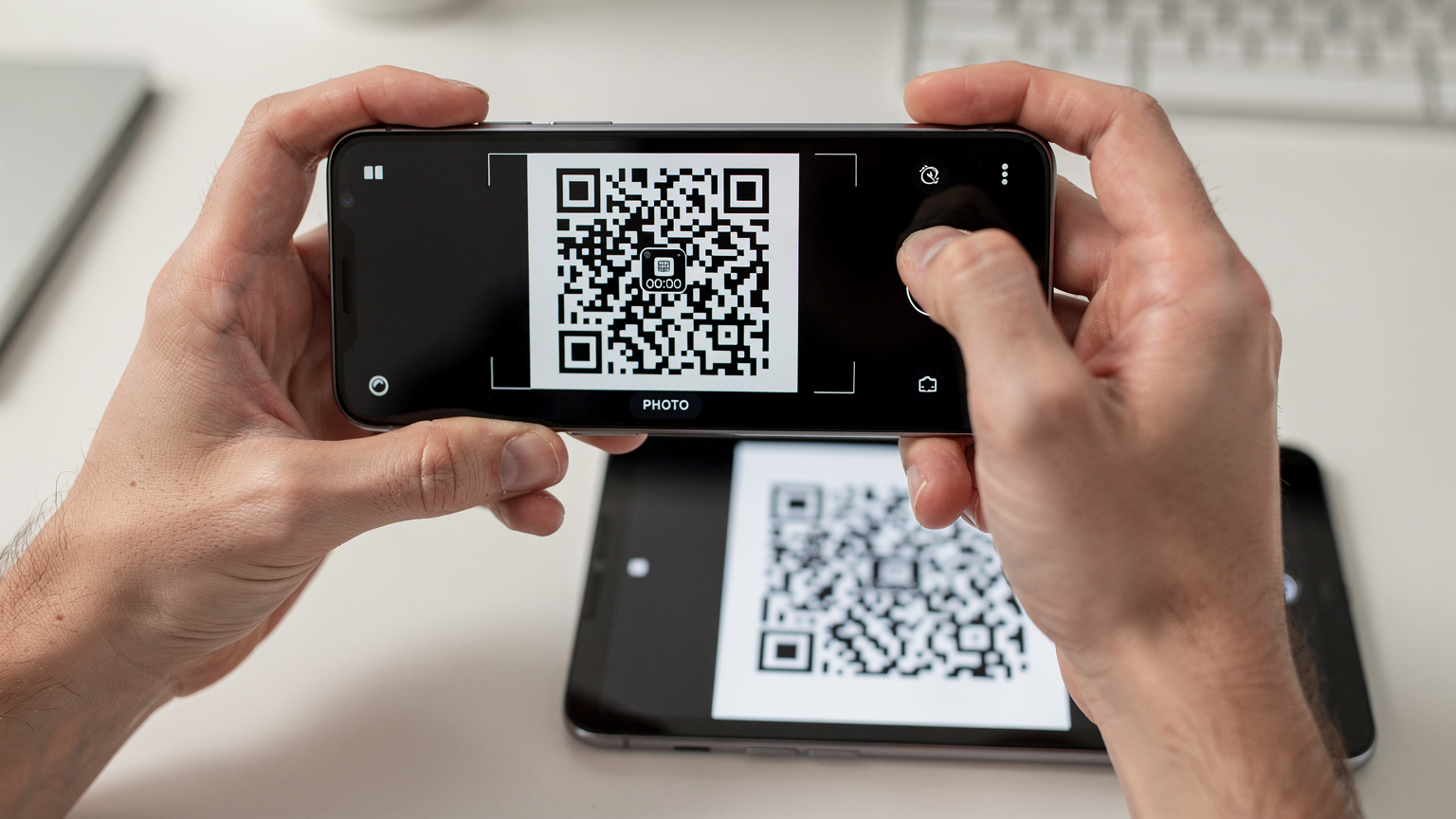 Duas mãos a segurar um smartphone a digitalizar um QR code exibido noutro dispositivo, para ativação do eSIM.