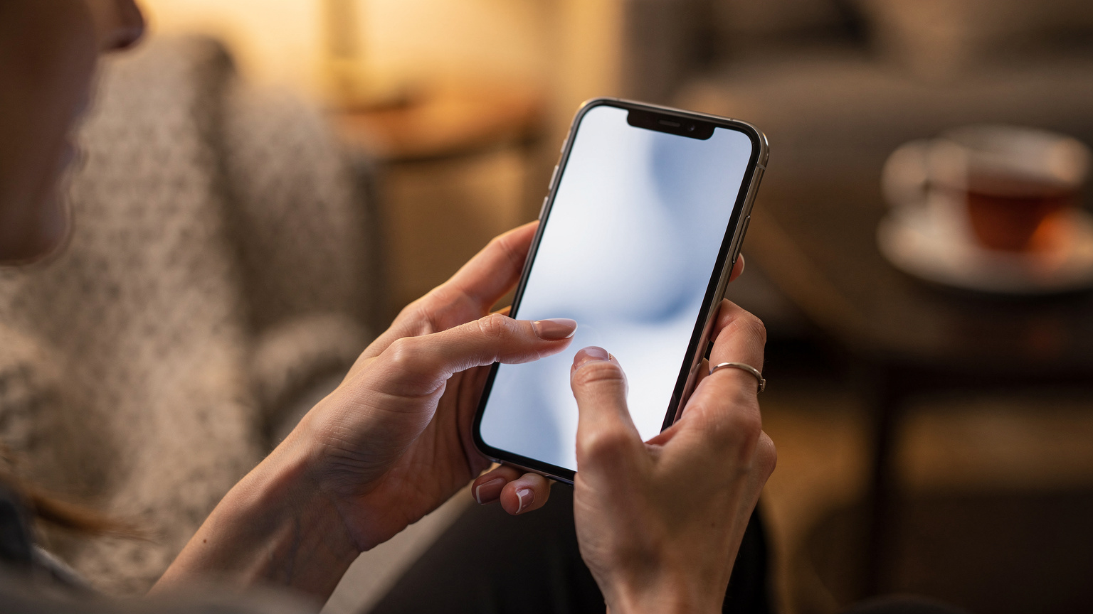 A close-up of human hands holding a smartphone, with a finger about to tap a confirmation button for eSIM activation, set against a blurred cozy home background.