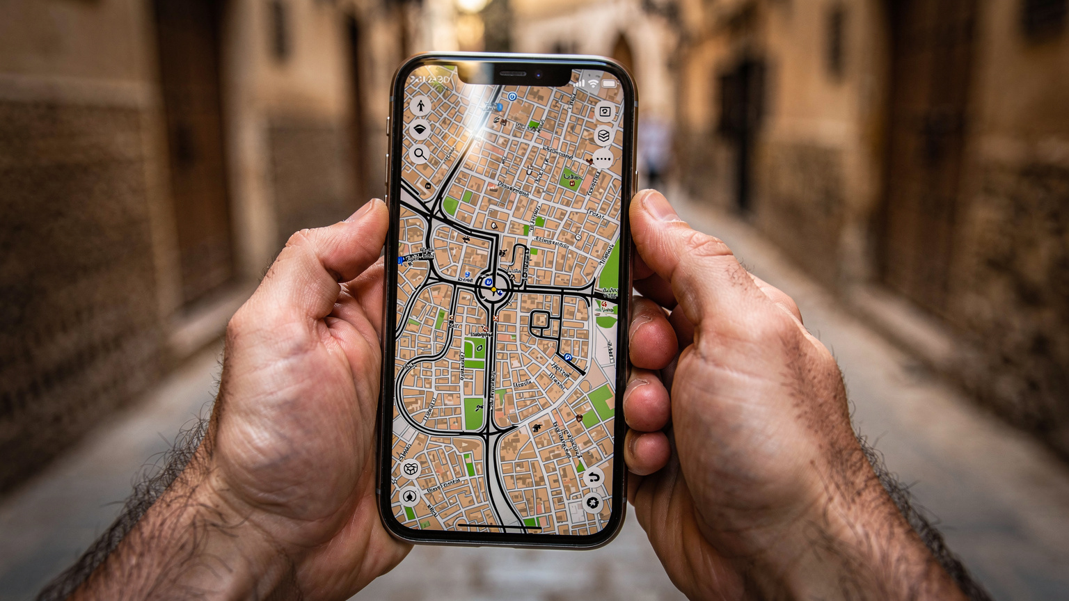 Zbliżenie na dłonie podróżnika trzymające smartfon, na ekranie którego wyświetla się aplikacja nawigacyjna z mapą medyny w Fezie, w tle rozmazane uliczki.