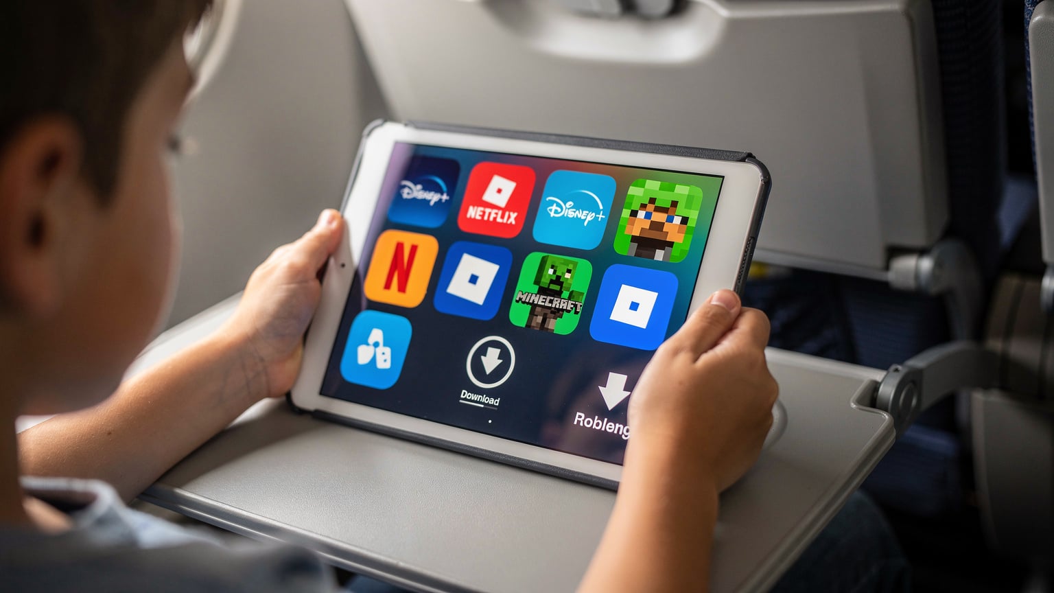 Детски ръце държат iPad, на екрана се виждат икони на популярни приложения за стрийминг и игри, с фокус върху бутона за изтегляне.