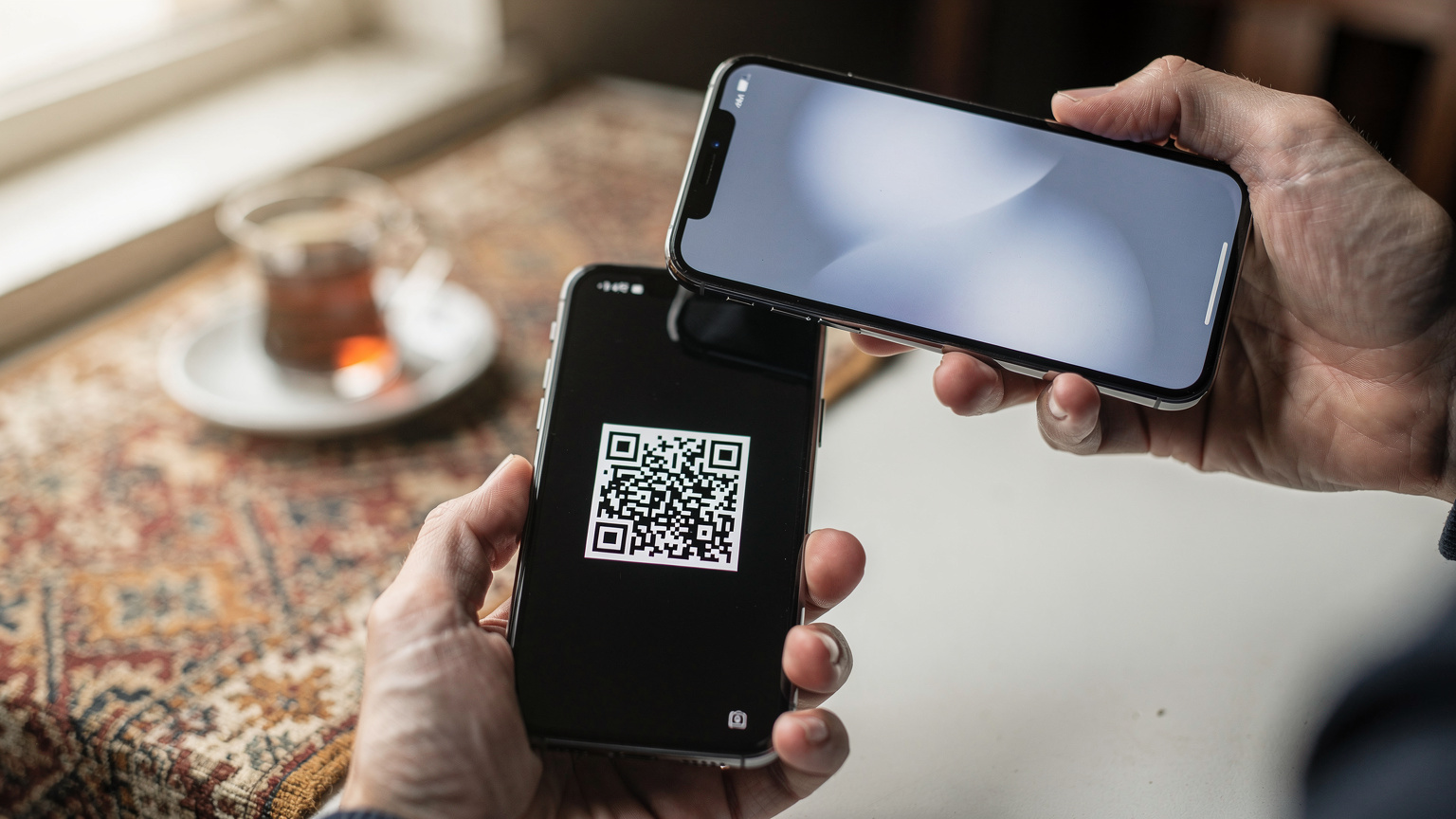 O mână apropiată a unei persoane scanează un cod QR de pe ecranul unui alt smartphone, demonstrând procesul rapid de activare a unui eSIM, cu o notificare de succes vizibilă pe ecranul receptor.