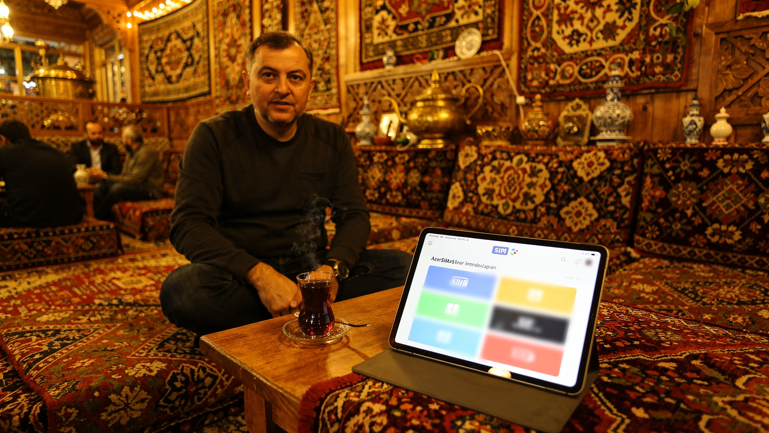 Eine Person sitzt in einem traditionellen Teeraum in Baku, Aserbaidschan, und vergleicht eSIM-Angebote auf einem Tablet.