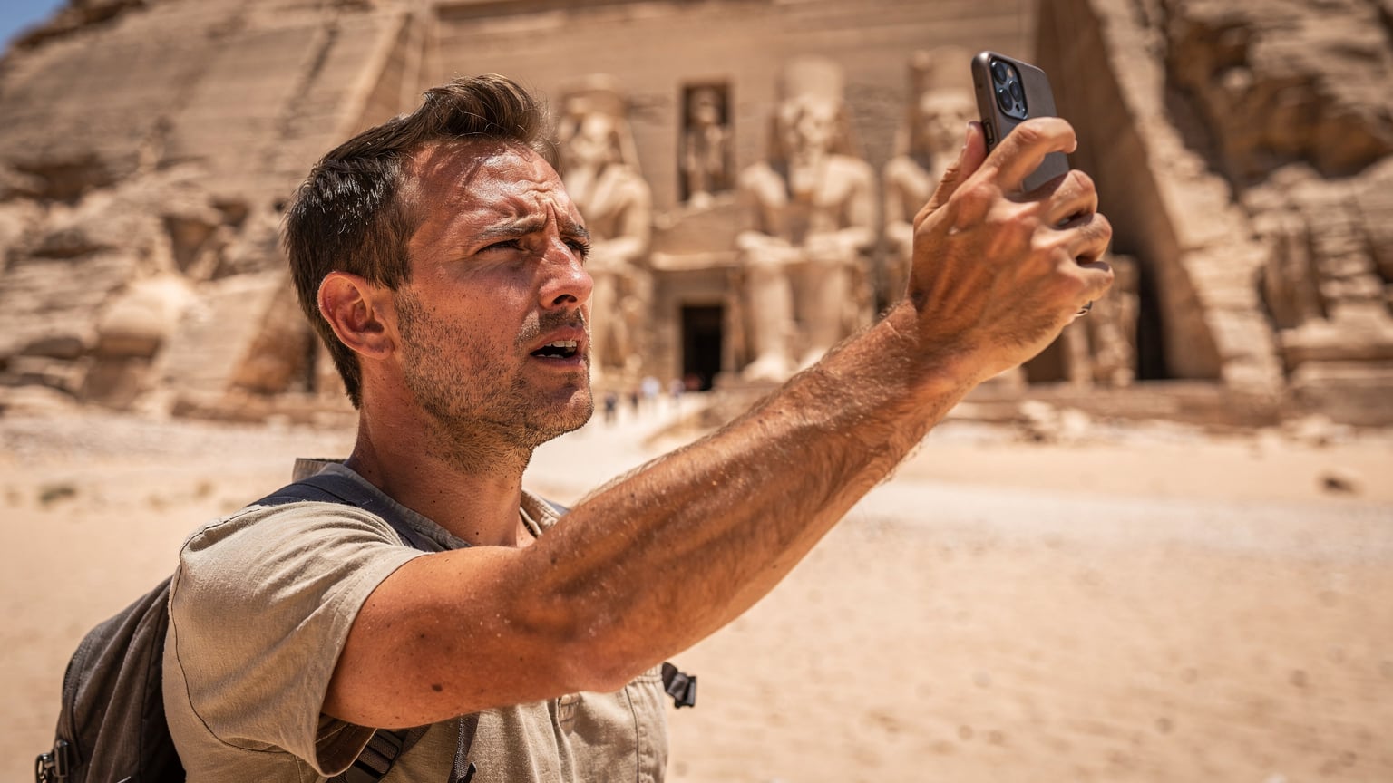 Un voyageur tente désespérément de capter du réseau sur son téléphone près des temples d'Abou Simbel, en Égypte, sous un soleil de plomb.