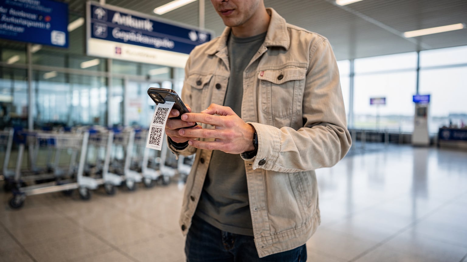 Eine Person am Münchner Flughafen, die mit ihrem Smartphone einen QR-Code scannt, um eine eSIM zu aktivieren, mit Gepäck und Flughafenschildern im Hintergrund.