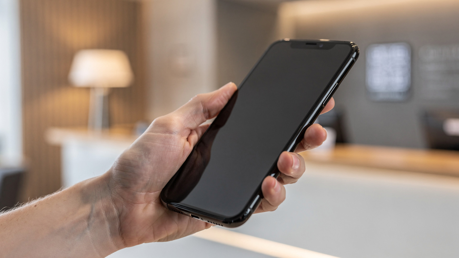 Nærbilde av en hånd som holder en smarttelefon og skanner en QR-kode for eSIM-aktivering, med en lett uskarp bakgrunn av et moderne hotellresepsjon-område i Oslo.