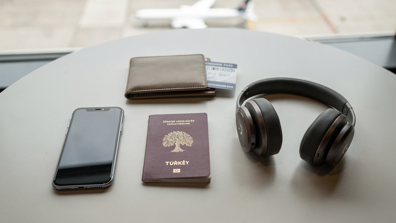 Yurt dışı havalimanında bir kafe masasında, pasaport, telefon ve kulaklık gibi seyahat aksesuarları düzgün bir şekilde yerleştirilmiş.