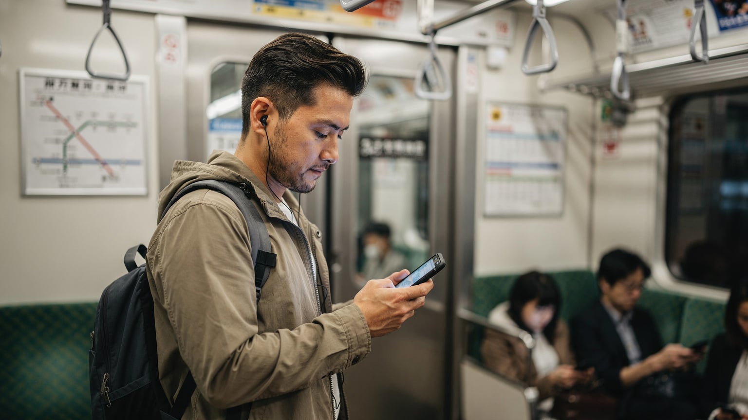 Un voyageur consulte son téléphone à l'intérieur d'un train de la ligne Yamanote à Tokyo, affichant une application de carte ou de transport. L'ambiance est calme et moderne.