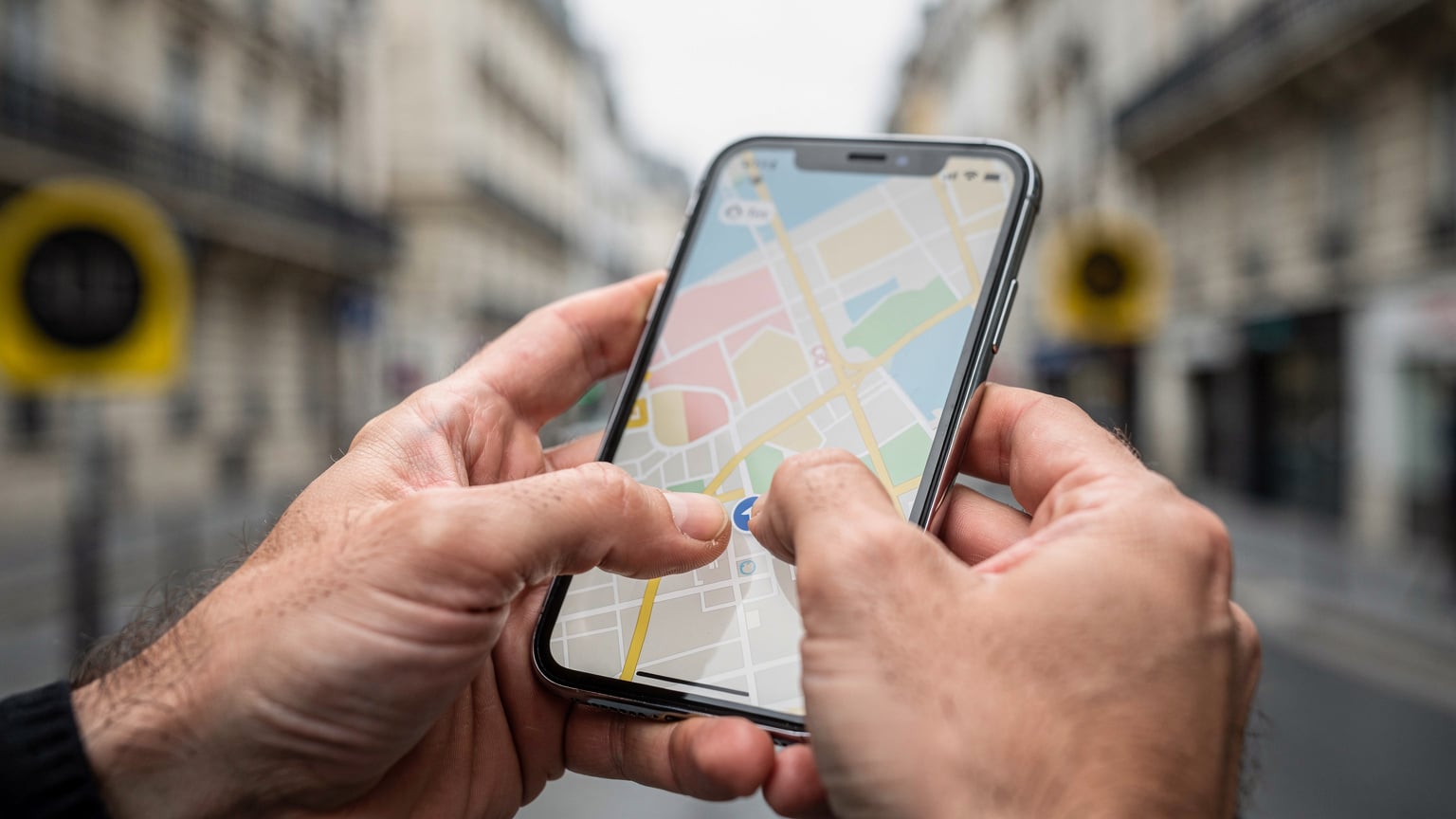 Detailní záběr na ruce cestovatele, který drží telefon s otevřenou mapovou aplikací a aktivní eSIM, s rozmazaným pozadím pařížské ulice s dopravními značkami.