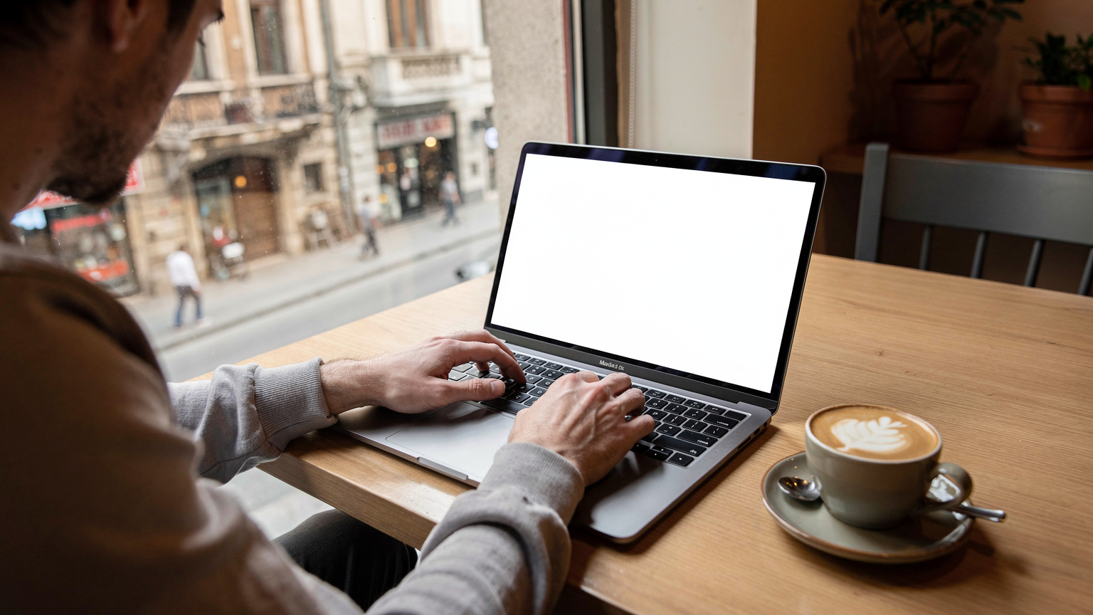 O persoană lucrează la un laptop într-o cafenea modernă din cartierul Kadıköy din Istanbul, cu o ceașcă de cafea artizanală pe masă și o fereastră mare cu vedere la strada aglomerată.