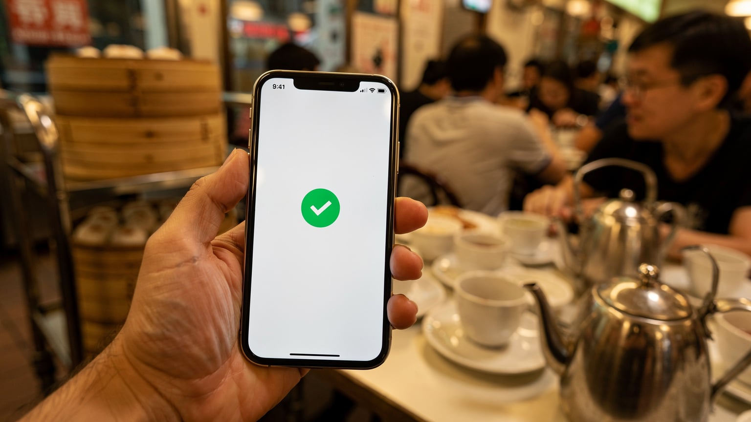 一只手拿着iPhone手机,屏幕上显示eSIM激活成功的界面,背景是香港街头一间茶餐厅的繁忙景象,暗示着游客已成功连接当地网络。