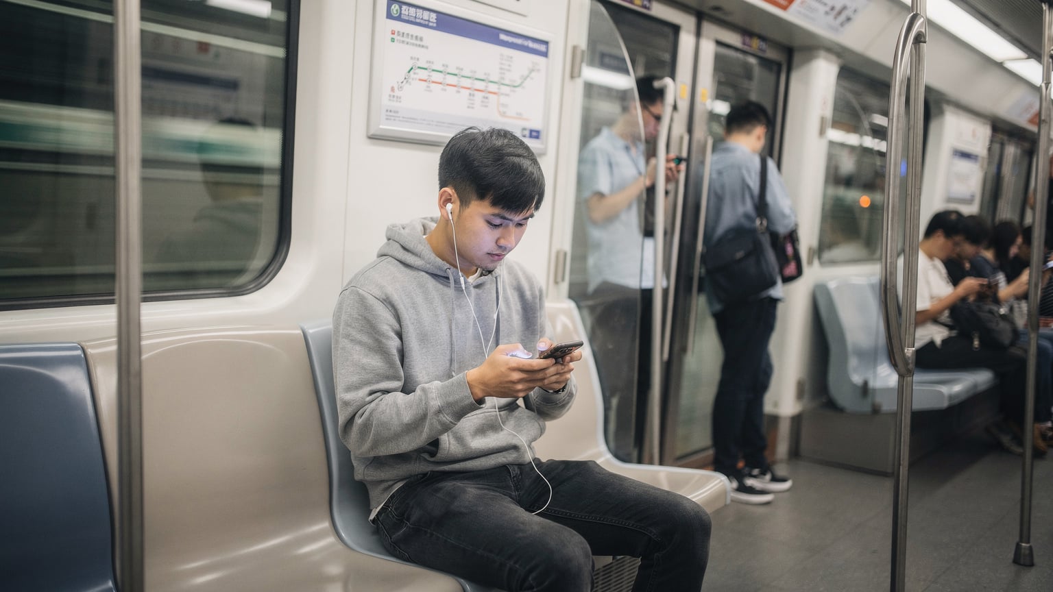 一名身著休閒服的年輕人,在上海地鐵車廂內專注地使用手機,車廂背景可見其他乘客。