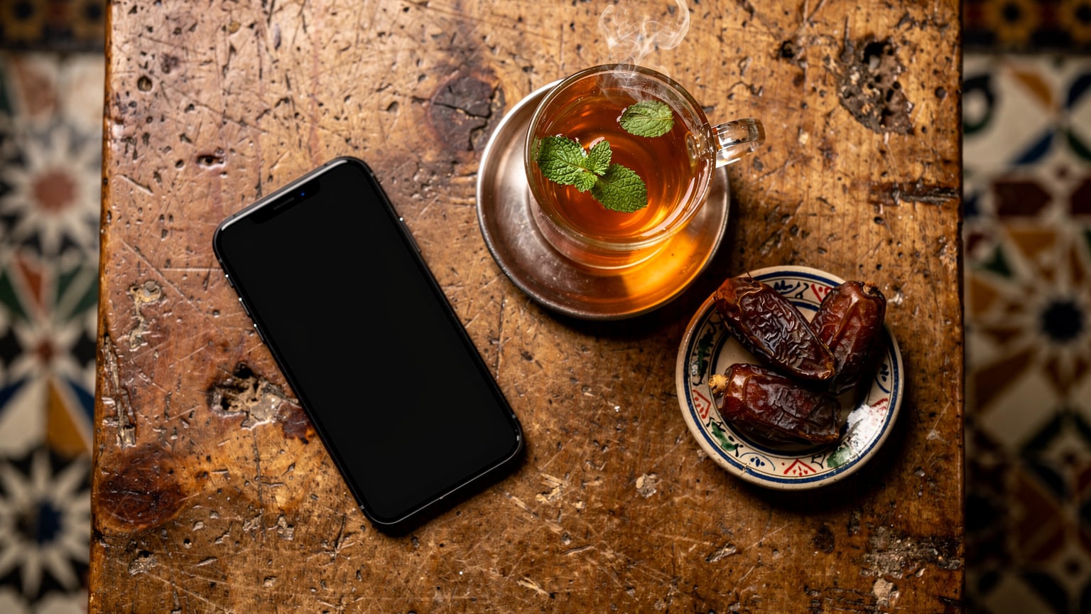 Vue aérienne d'un smartphone sur une table de café en bois, avec une tasse de thé à la menthe égyptien et des dattes à côté, illustrant la pause connectée.