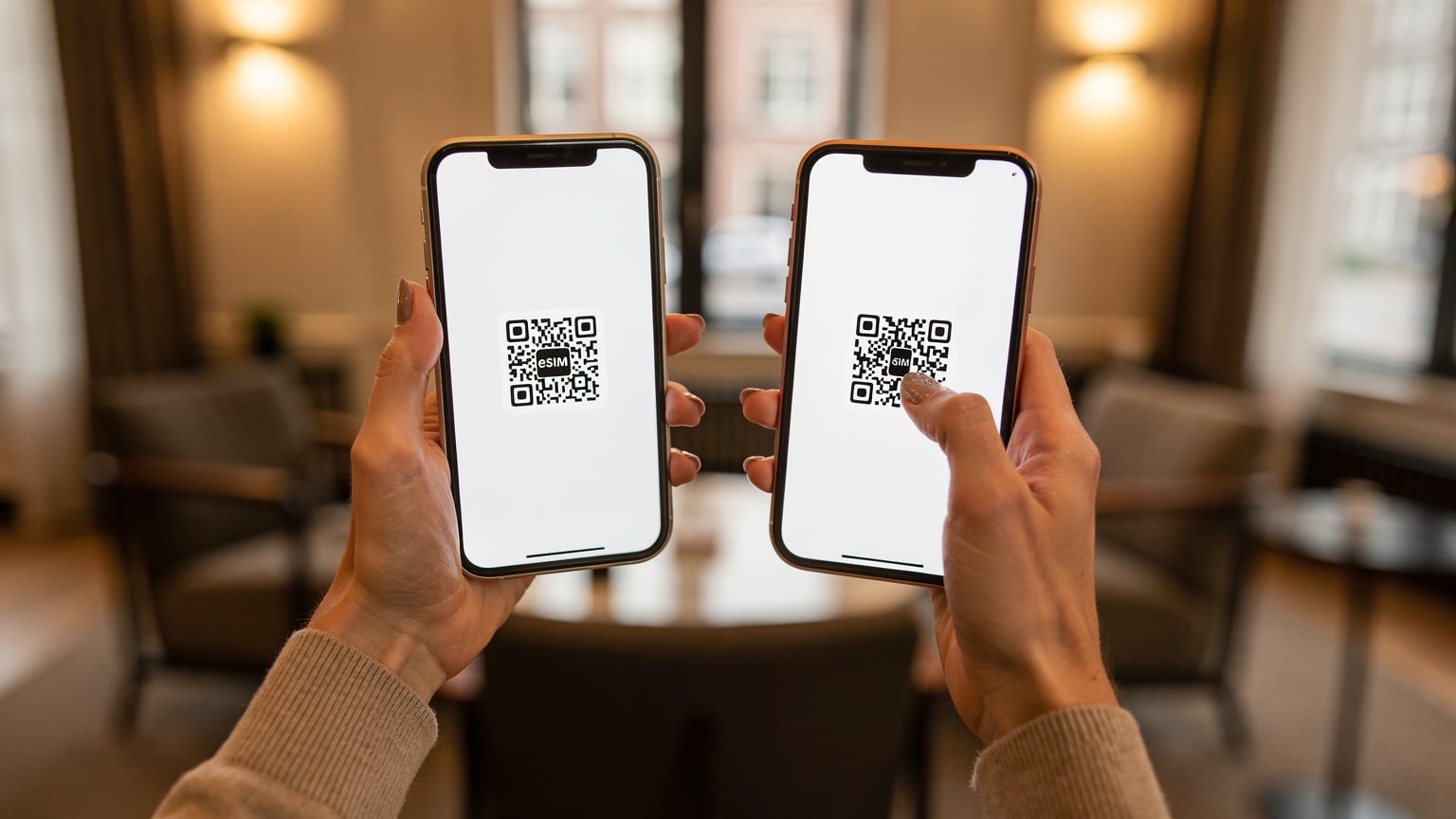 Tangan seorang wanita memegang ponsel iPhone, sedang memindai kode QR untuk mengaktifkan eSIM di lobi hotel yang tenang di Amsterdam.