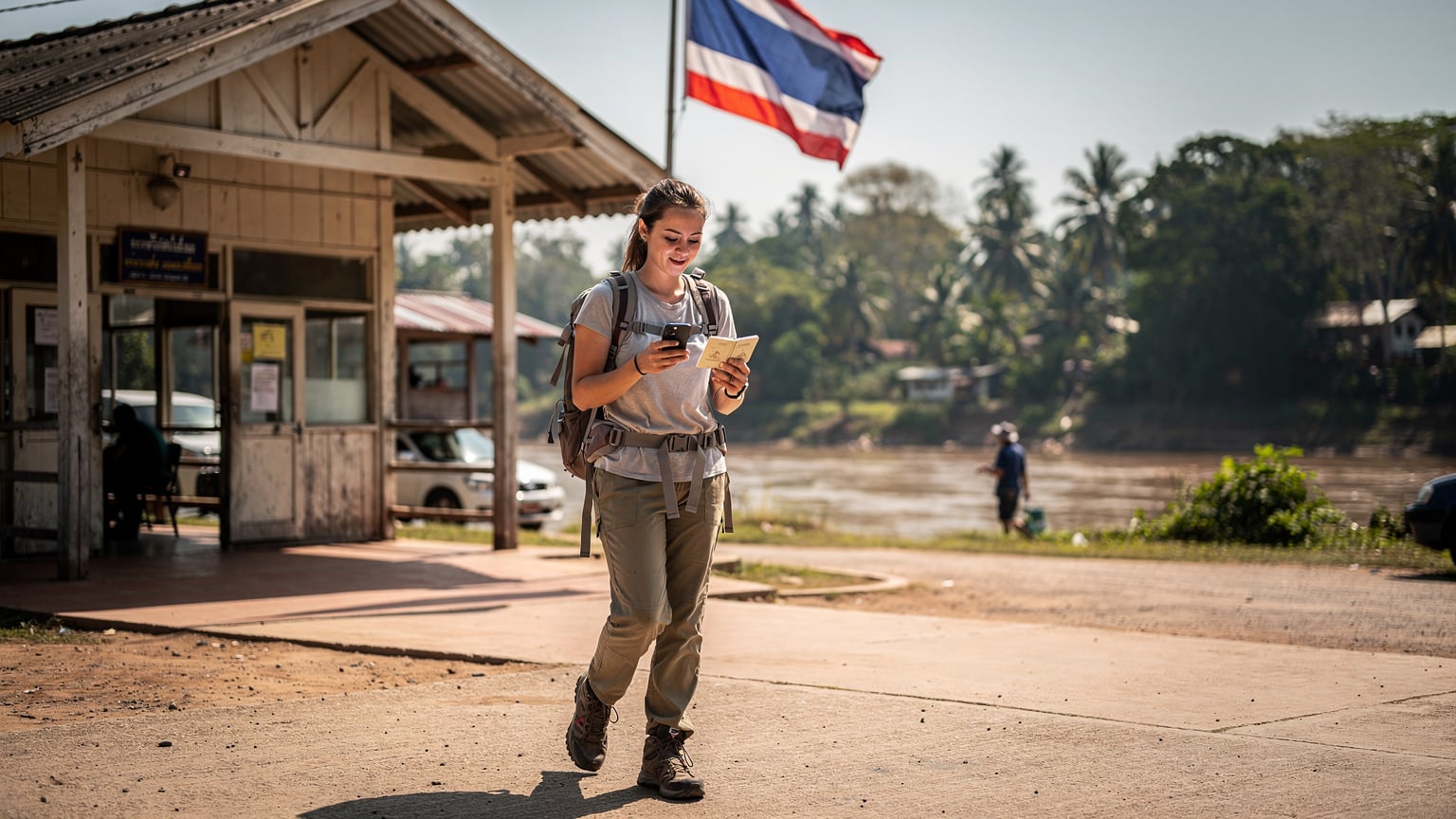 タイとラオスを結ぶメコン川の国境検問所で、パスポートとiPhoneを手に、スムーズな入国手続きを済ませるバックパッカーの女性。