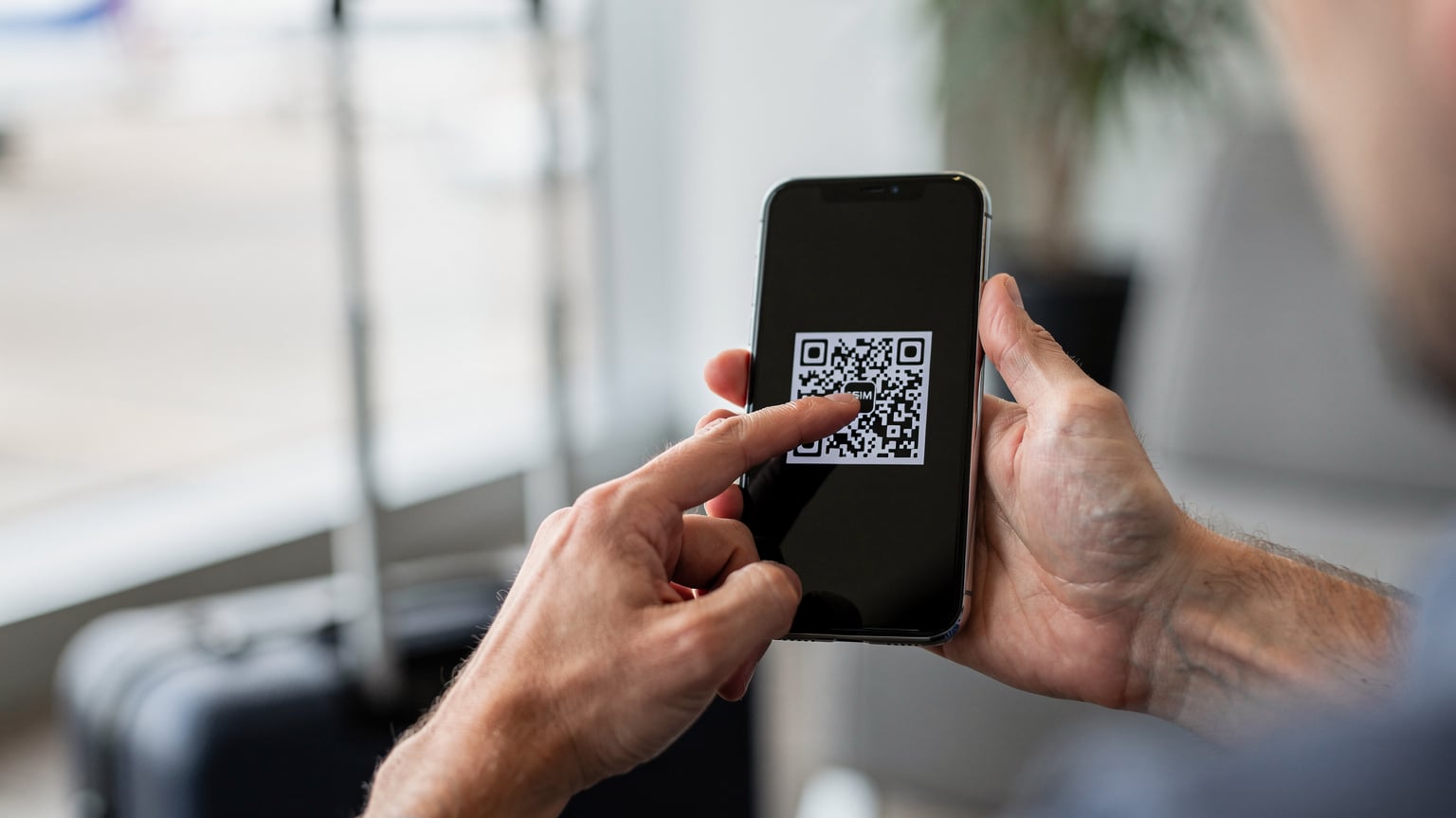 Путешественник легко сканирует QR-код для активации eSIM на своем смартфоне в комфортной обстановке, избегая очередей в аэропорту.